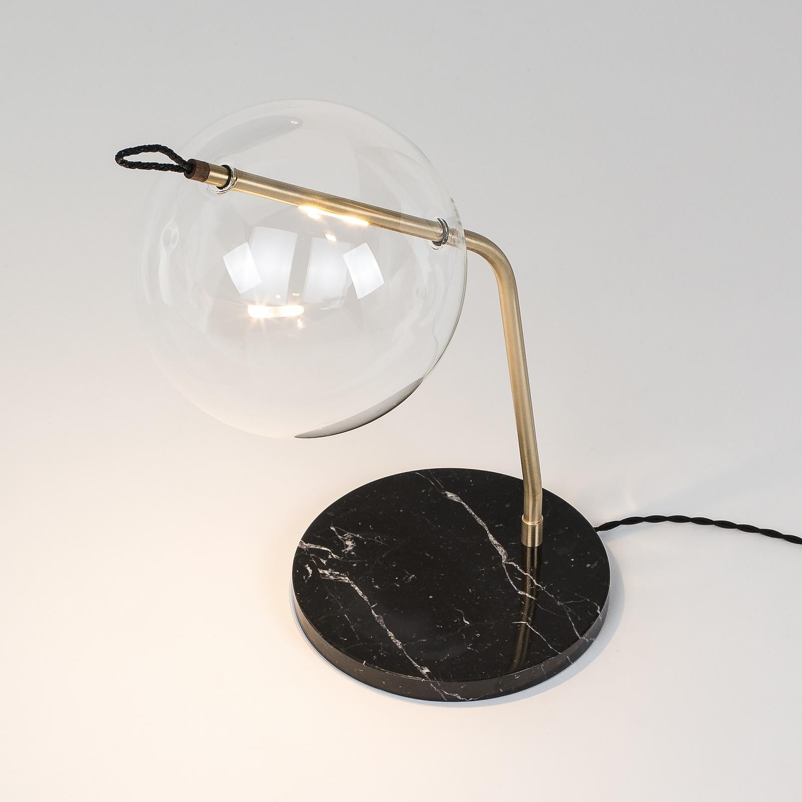 The clear glass sphere of this modern table lamp, delicately held in place by a golden brass stem, provides a diffused illumination that is suitable for desks and side tables in both modern and contemporary interiors. Unique and captivating, this