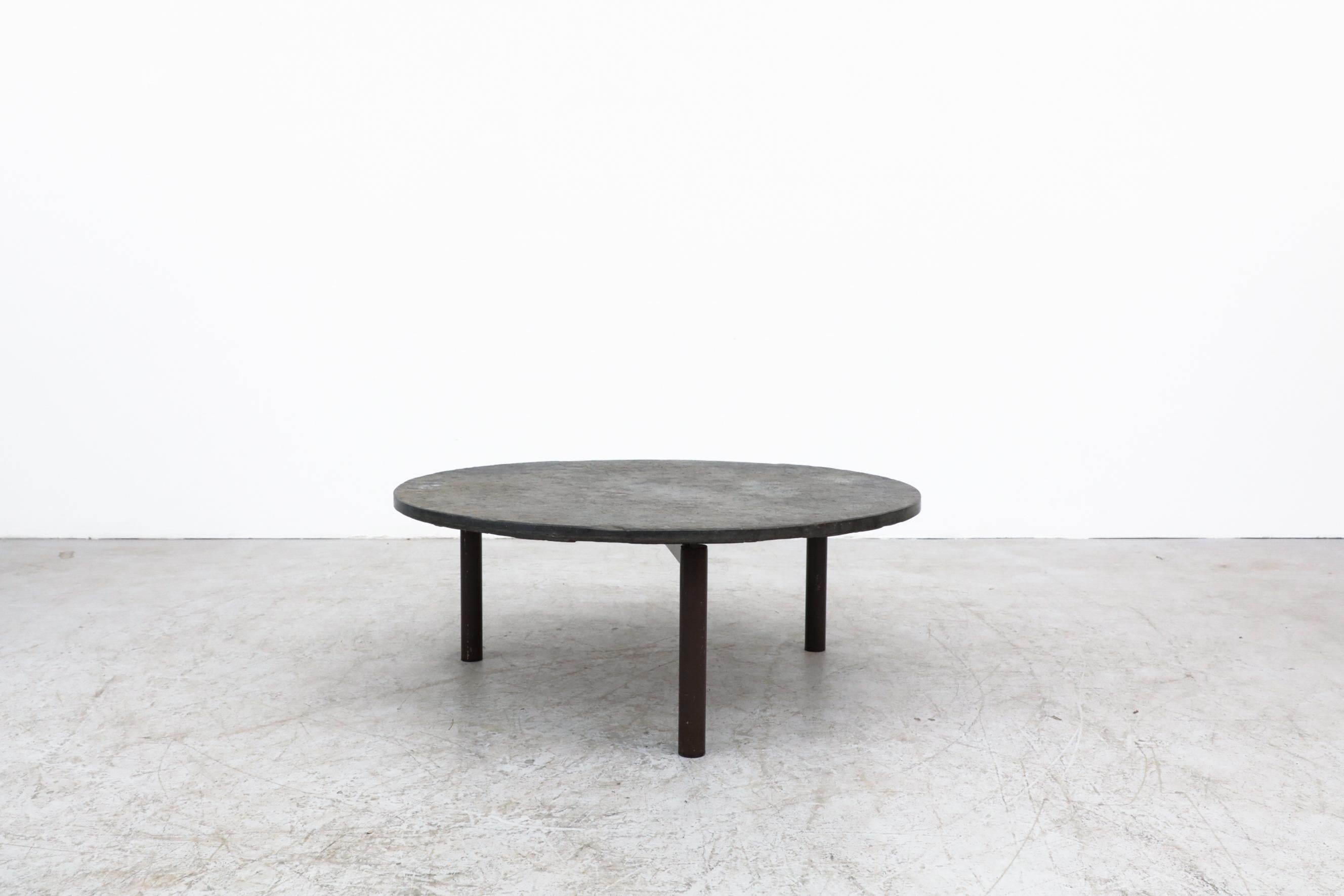 't Spectrum round stone coffee table with brown enameled tripod base. Heavy stone slab top with even grey tone. Stone has some scratching and chipping. The base has visible scratches as well. Bolts in the frame top act as leveling tools. In original