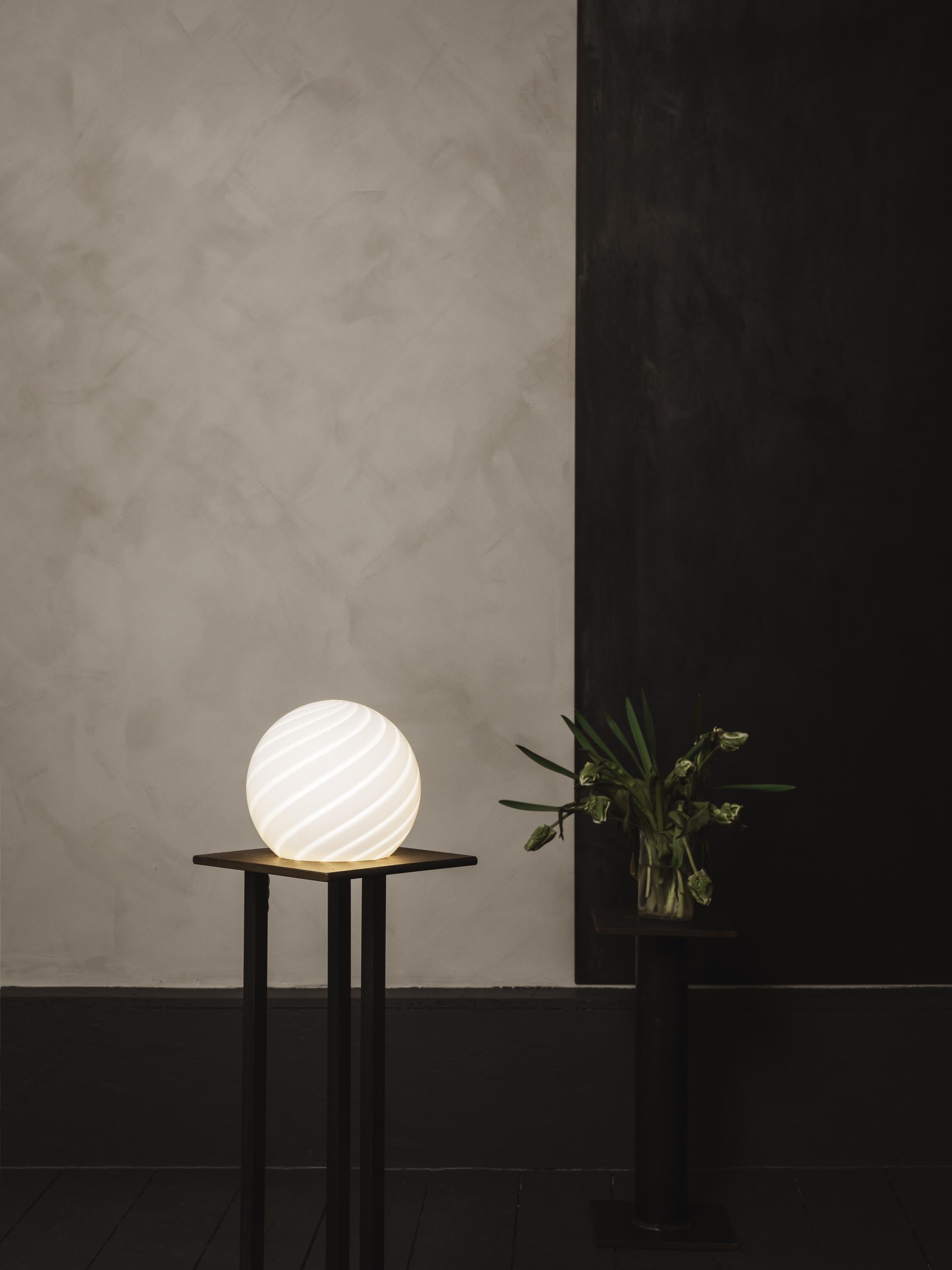 Sphere-shaped table lamp crafted from mouth-blown opaline glass. The design
features a swirl pattern obtained using an original 1970s mould, specifically picked to give the lamp a clean expression. The piece includes hand-casted brass