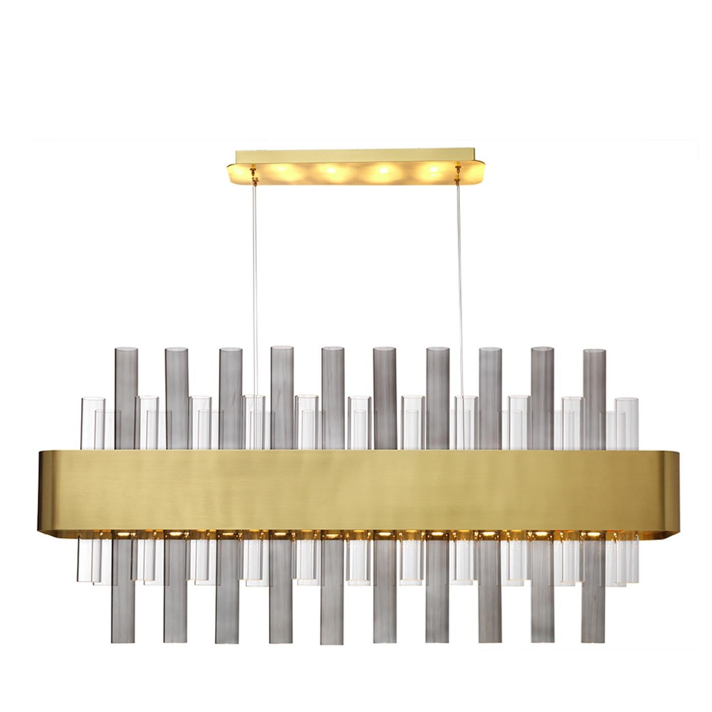 Create a chic atmosphere in a contemporary dining space with the tab chandelier. Drawing inspiration from different eras and styles, the chandelier features a brass body with a satin finish that envelops transparent and smoky crystal elements. The