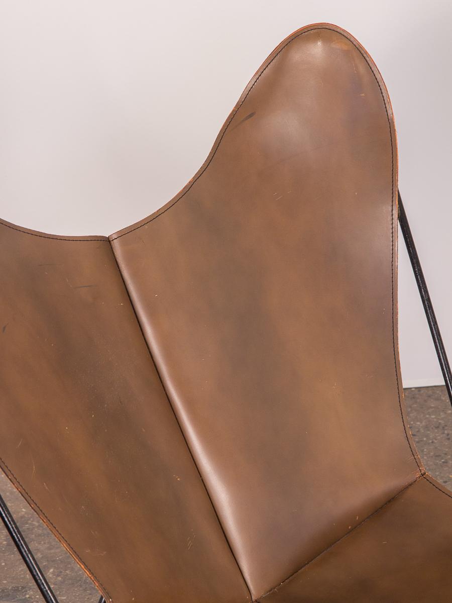 Vintage tabacco leather Hardoy Butterfly chair for knoll. A classic accent chair whose design is effortlessly minimal. Our 1960s example has a thick, smoky tabacco leather sling that is supple and robust, with a gorgeous patina. Black enamel frame