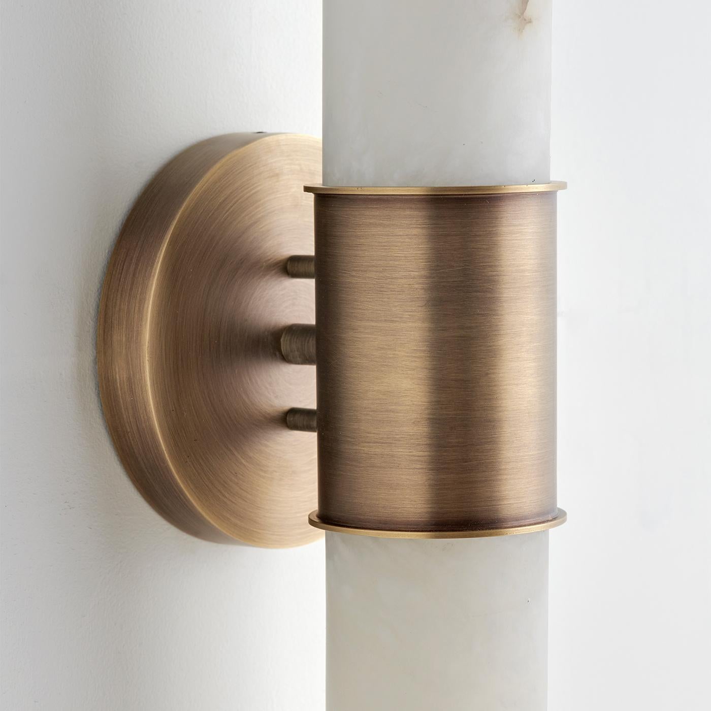 La Lámpara de Pared Tabitha fusiona a la perfección la elegancia atemporal del alabastro con el atractivo moderno del latón cepillado. Sus característicos tubos de alabastro cortados en diagonal en forma de 