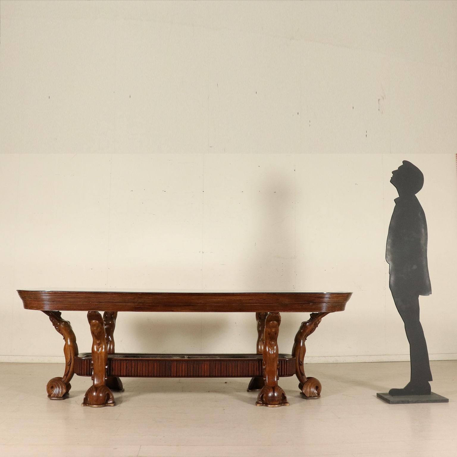 Table with wooden structure and supporting sculptural elements, glass top and planter in the base.