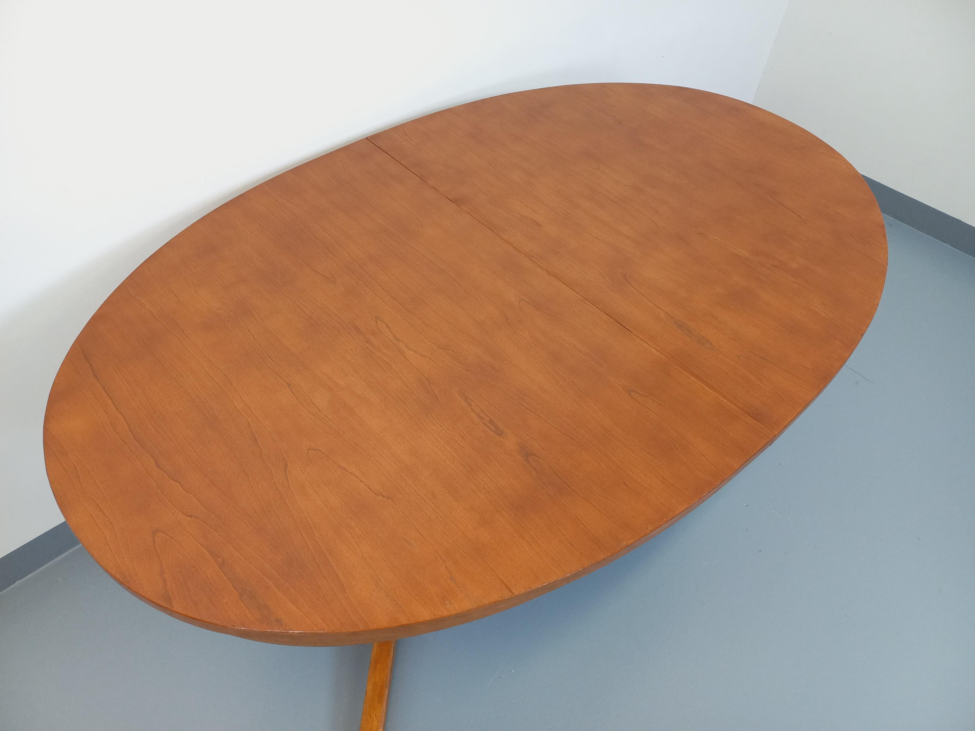 Table à manger vintage des années 60 70, de la manufacture française Baumann, de style scandinave et de forme ovale, beau plateau en orme clair, 2 pieds centraux à 4 branches en orme. La table s’ouvre par le centre pour accueillir deux rallonges en