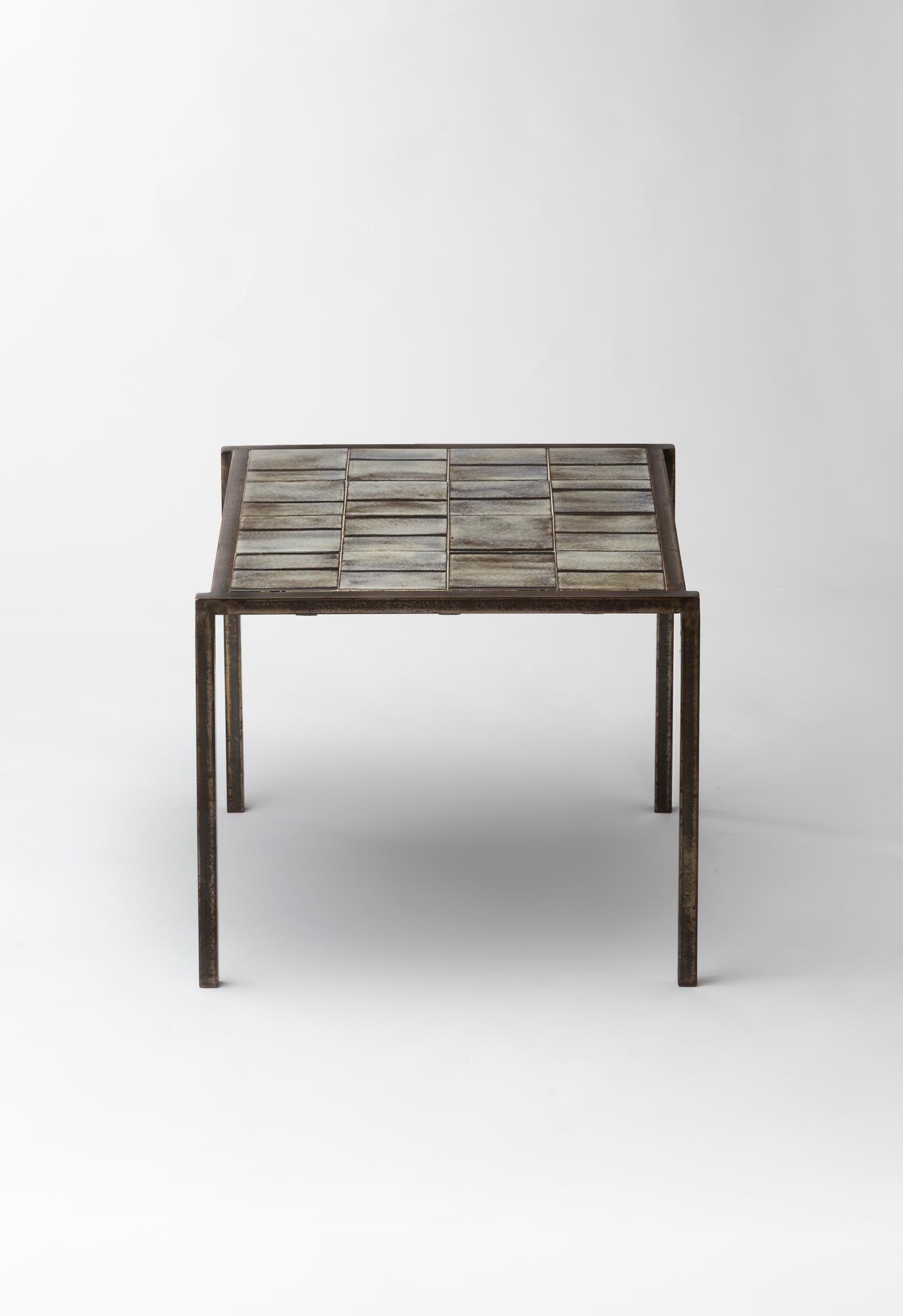 Cette table basse carrée de Mado Jolain, créée dans les années 1960, incarne l'élégance à la fois brute et poétique de son travail. Sa base métallique fine et géométrique supporte un plateau décoré de carreaux de céramique émaillée, disposés dans
