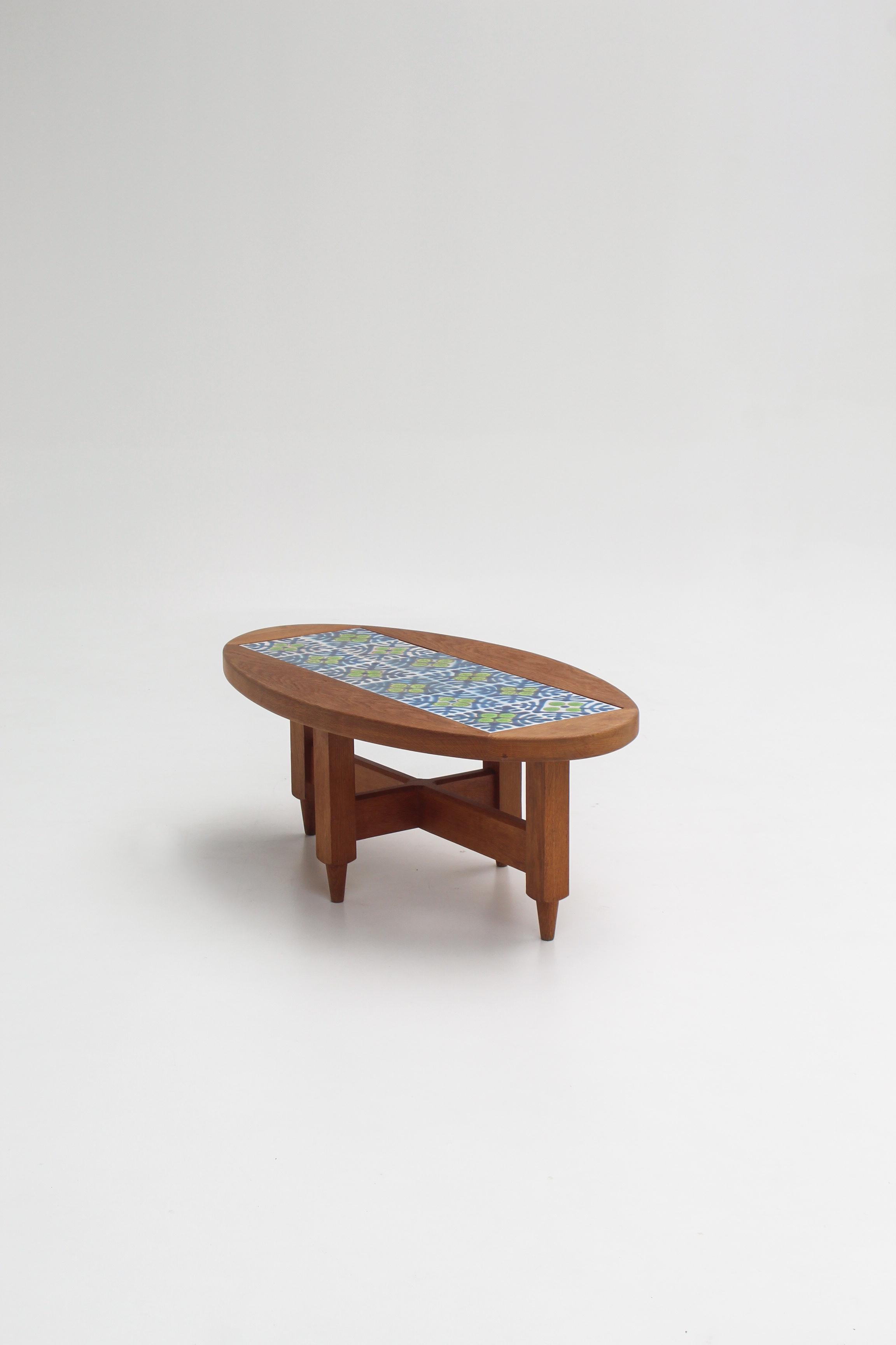 Table basse ovale signée Guillerme & Chambron pour l'éditeur Votre Maison, France, années 1960.
La structure en chêne massif typique du duo dialogue ici avec un plateau en carreaux de céramique colorés, aux motifs géométriques verts, bleus et