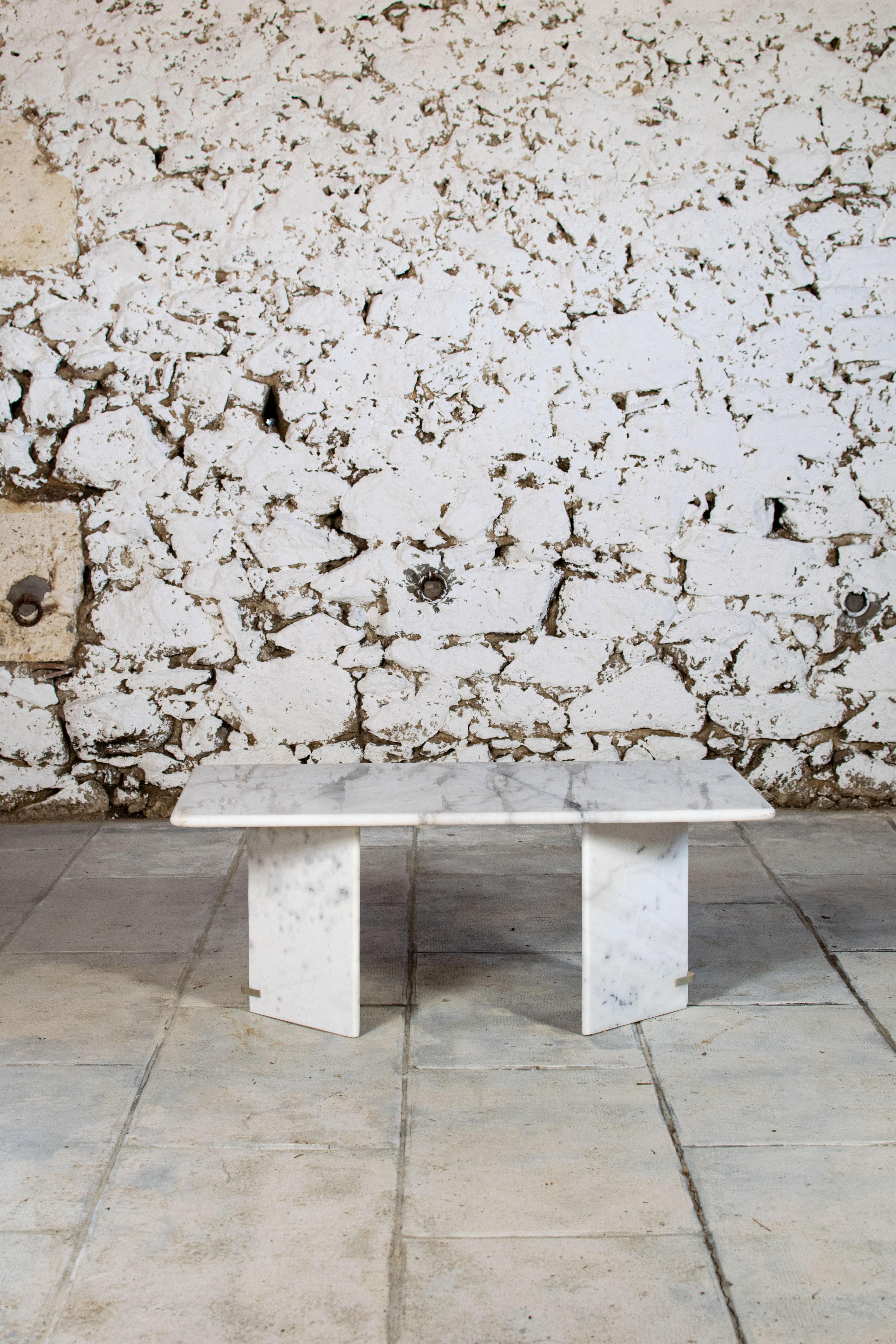 Table basse en marbre blanc des années 1970. Le plateau repose sur deux pieds en forme d'angle. 