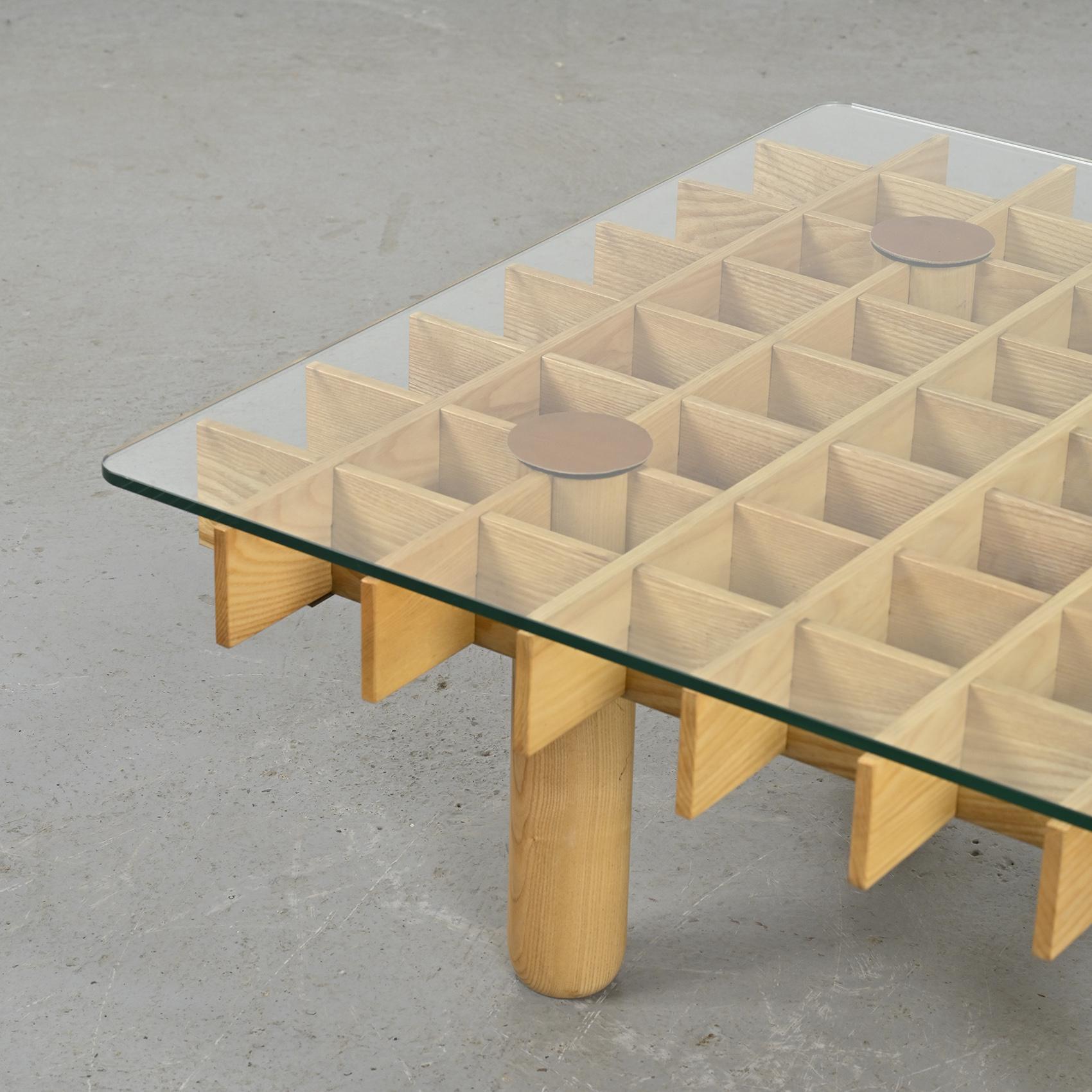 A graphic square coffee table designed by Gianfranco Frattini.

The structure is made up of turned ash wood legs and slats. The crystal top rests on four fawn-coloured vegetal leather discs.

Manufacturer: Ghianda, circa 1974.
