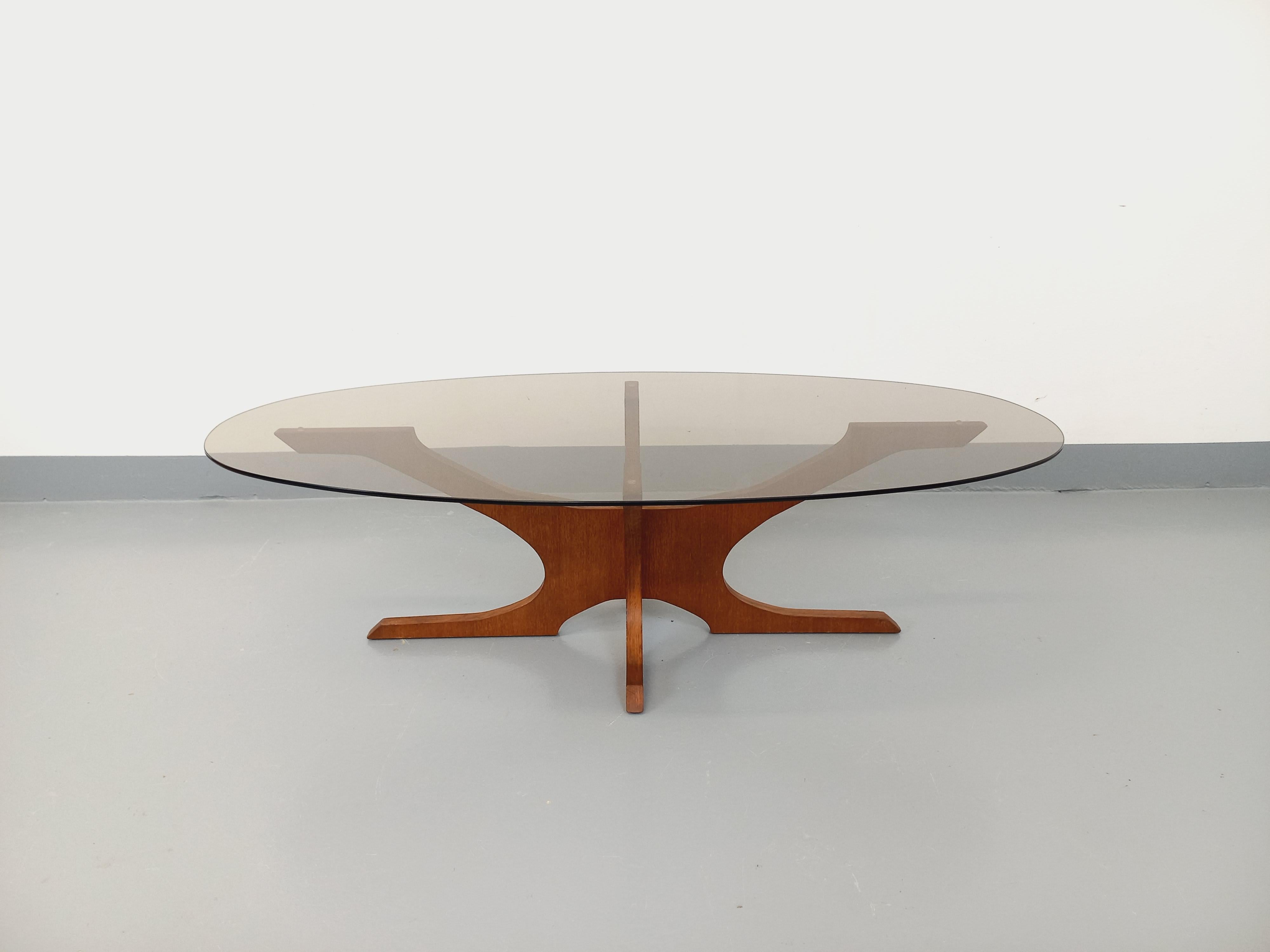 Table basse ovale vintage des années 60 70, attribuée au designer Hugues Poignant, pied design en teck, plateau ovale en verre fumé épais, bon état général avec des micro-rayures de surface sur le plateau en verre, et des restaurations effectuées