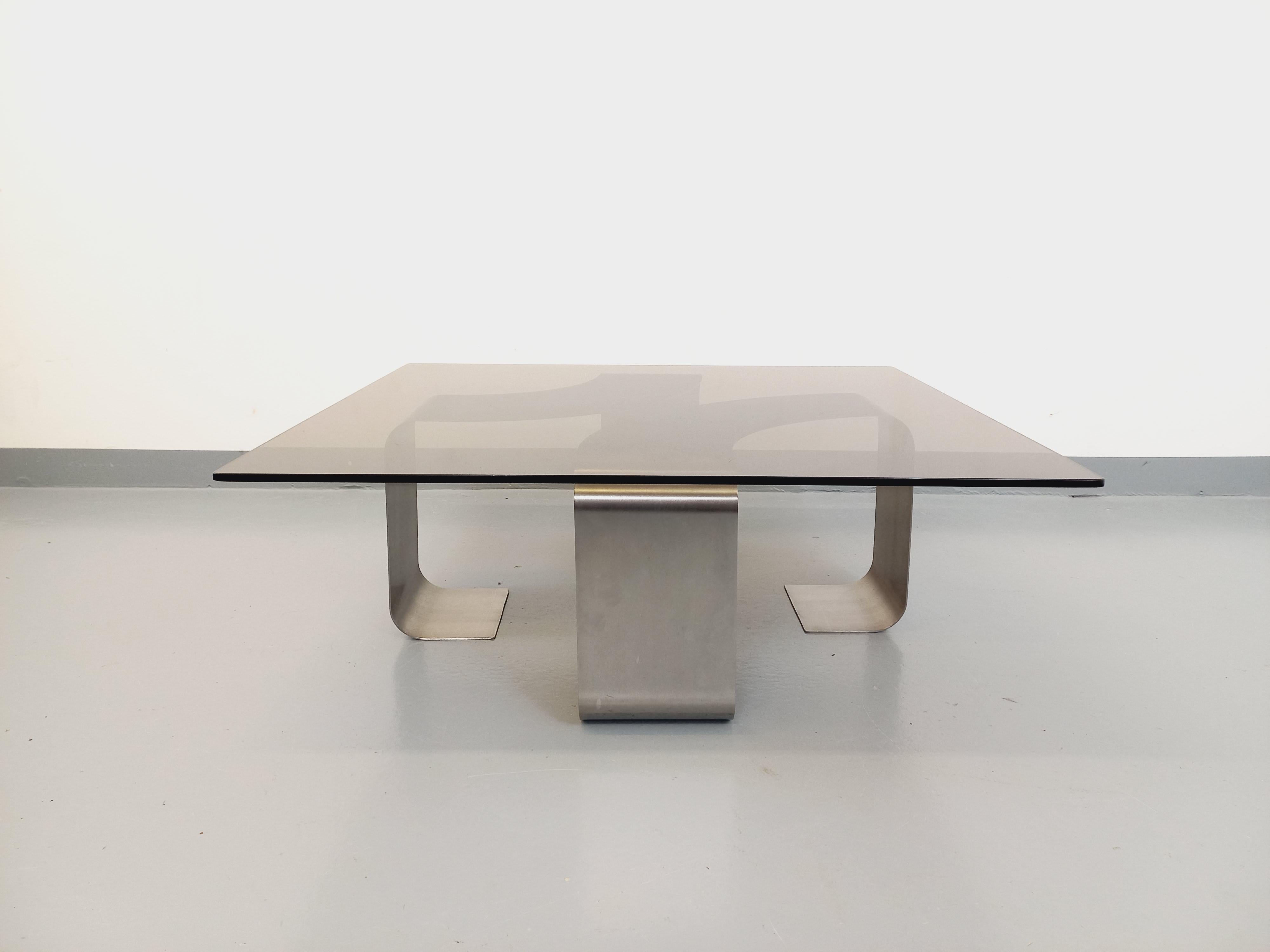 Grande table basse vintage des années 70, attribuée au designer français François Monnet, style Space Age, piétement design en acier brossé plié et courbé, grand plateau rectangulaire quasiment carré aux angles arrondis en verre fumé. Design/One,