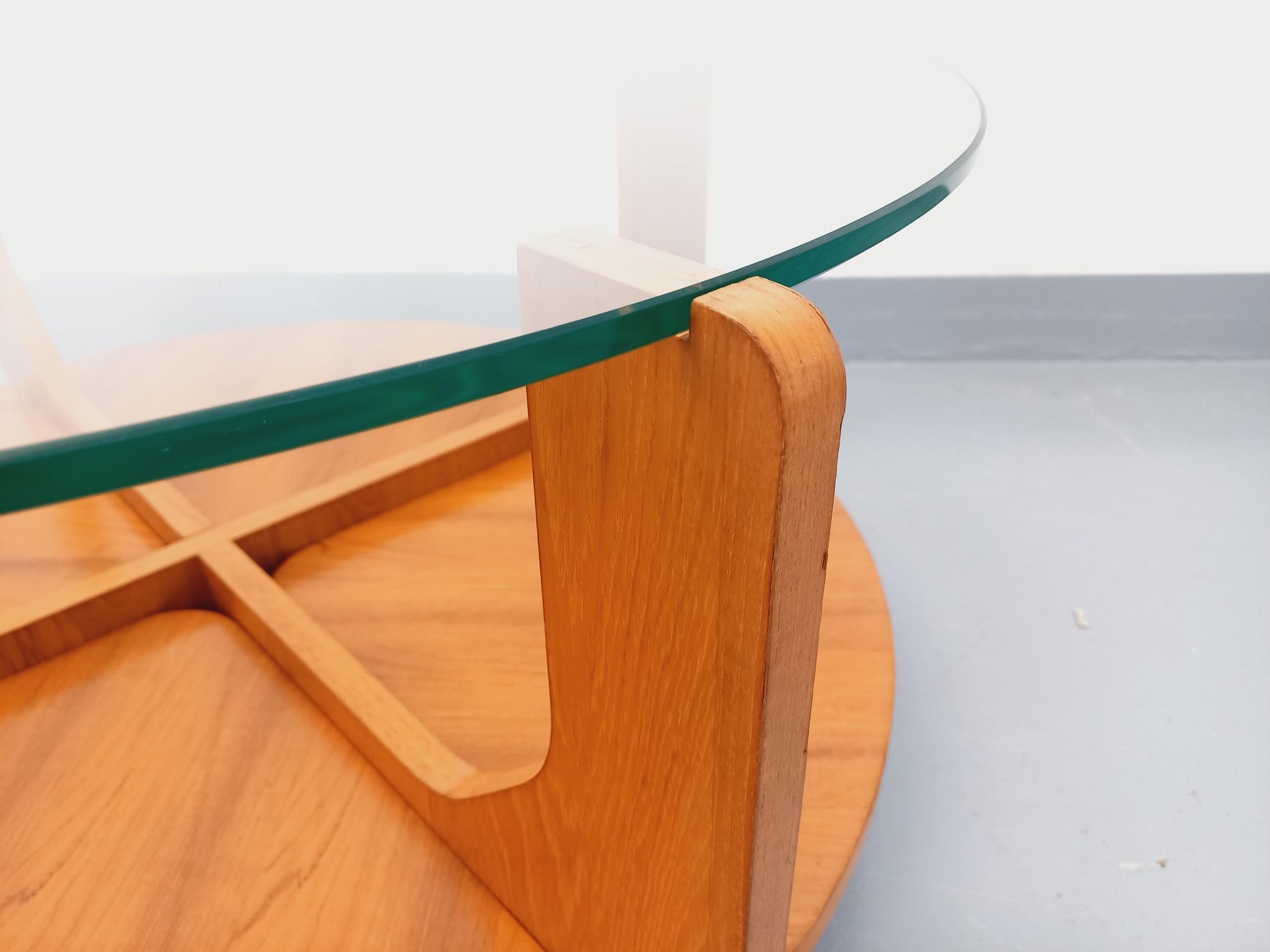 Table basse ronde vintage des années 60 70, du designer Hugues Poignant, pied en teck, plateau supérieur en verre transparent rond, plateau inférieur porte-revue en teck, très beau design. Très bon état général avec quelques rares micro-rayures de