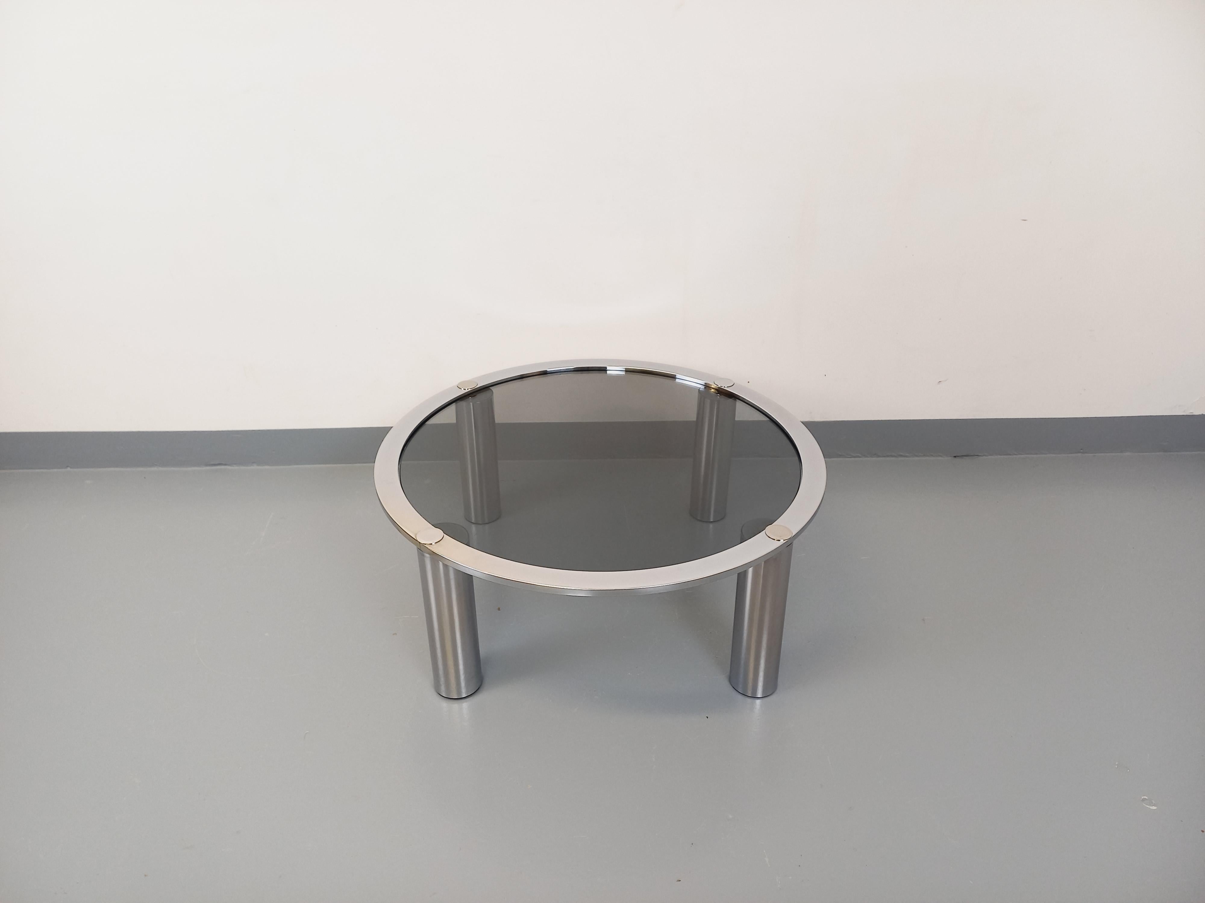 Table basse ronde vintage des années 70, style Space Age, probablement de chez Roche Bobois, plateau en verre fumé, piétement en métal chromé à 4 pieds cylindriques. Très bon état général avec quelques signes du temps qui passe et quelques