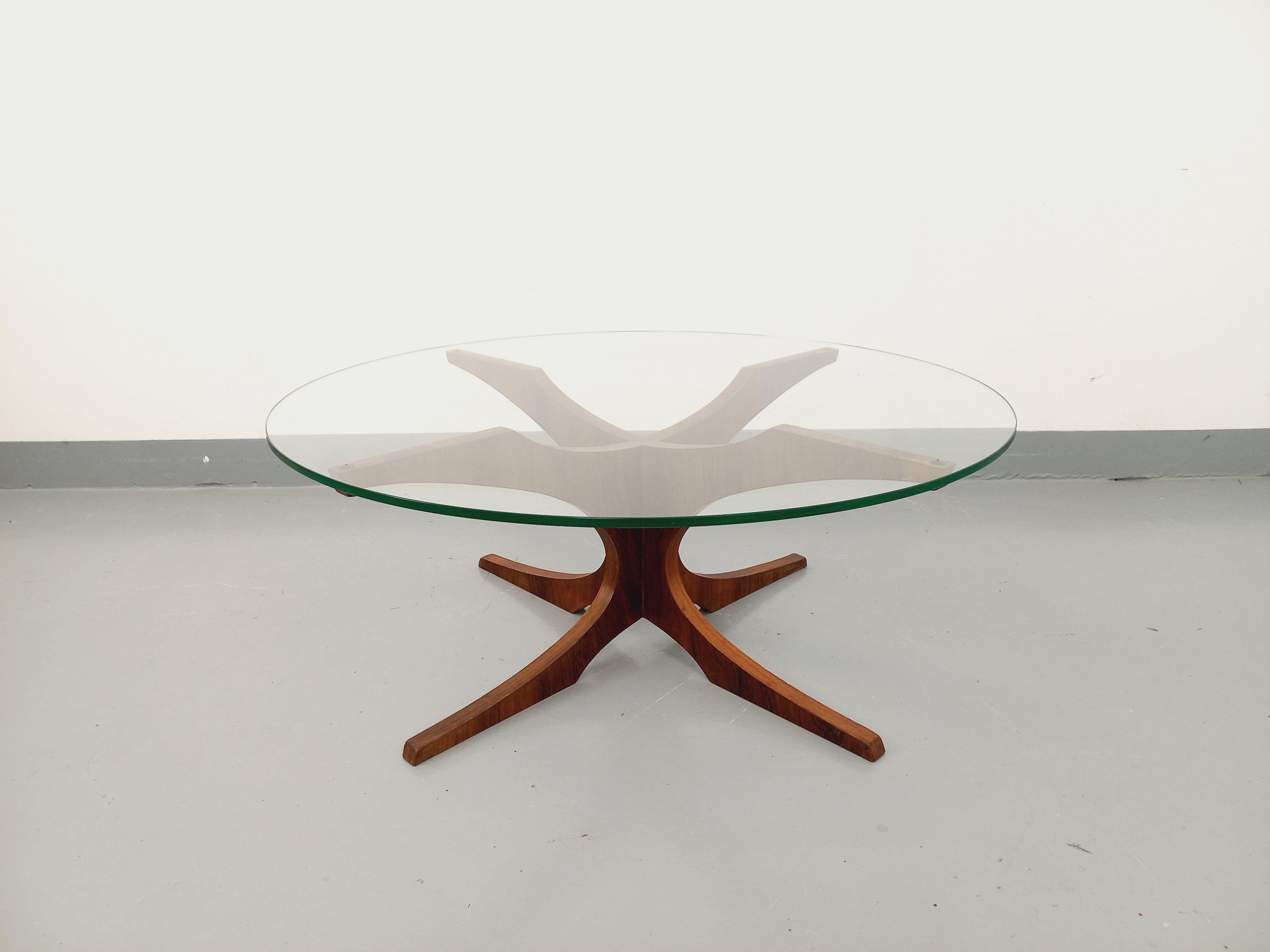 Table basse ronde vintage des années 60 70, attribuée au designer Hugues Poignant, pied design en palissandre, plateau rond en verre transparent épais, bon état général avec quelques rayures de surface sur le plateau en verre, et 2 petits éclats au