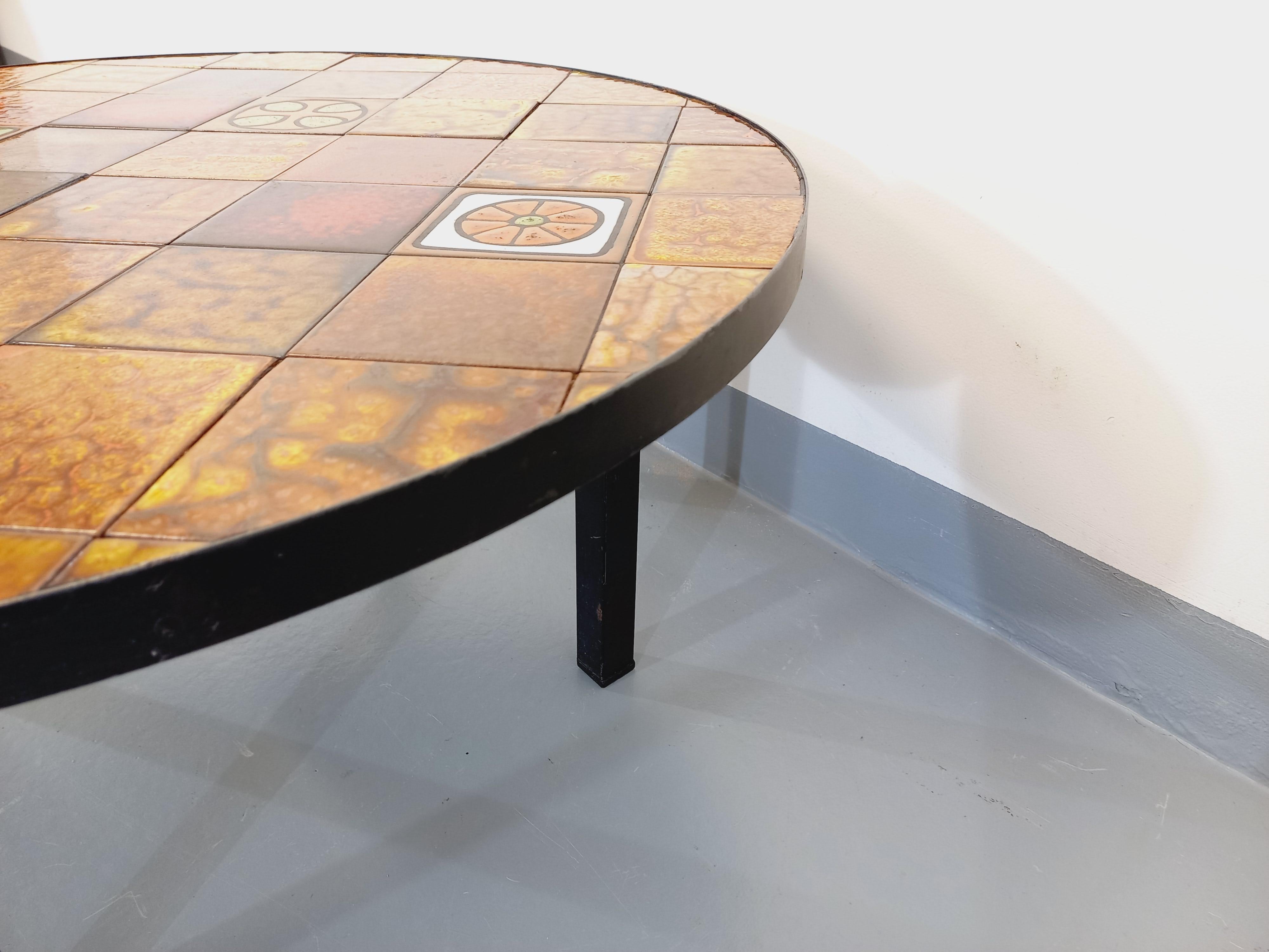 Table basse ronde vintage des années 70, attribuée à la marque Roche-Bobois, piétement et structure en métal noir, plateau en céramique de Vallauris à motifs colorés dans les tons ocres et orangés (ocre, jaune, orange, rouge, blanc, vert amande).