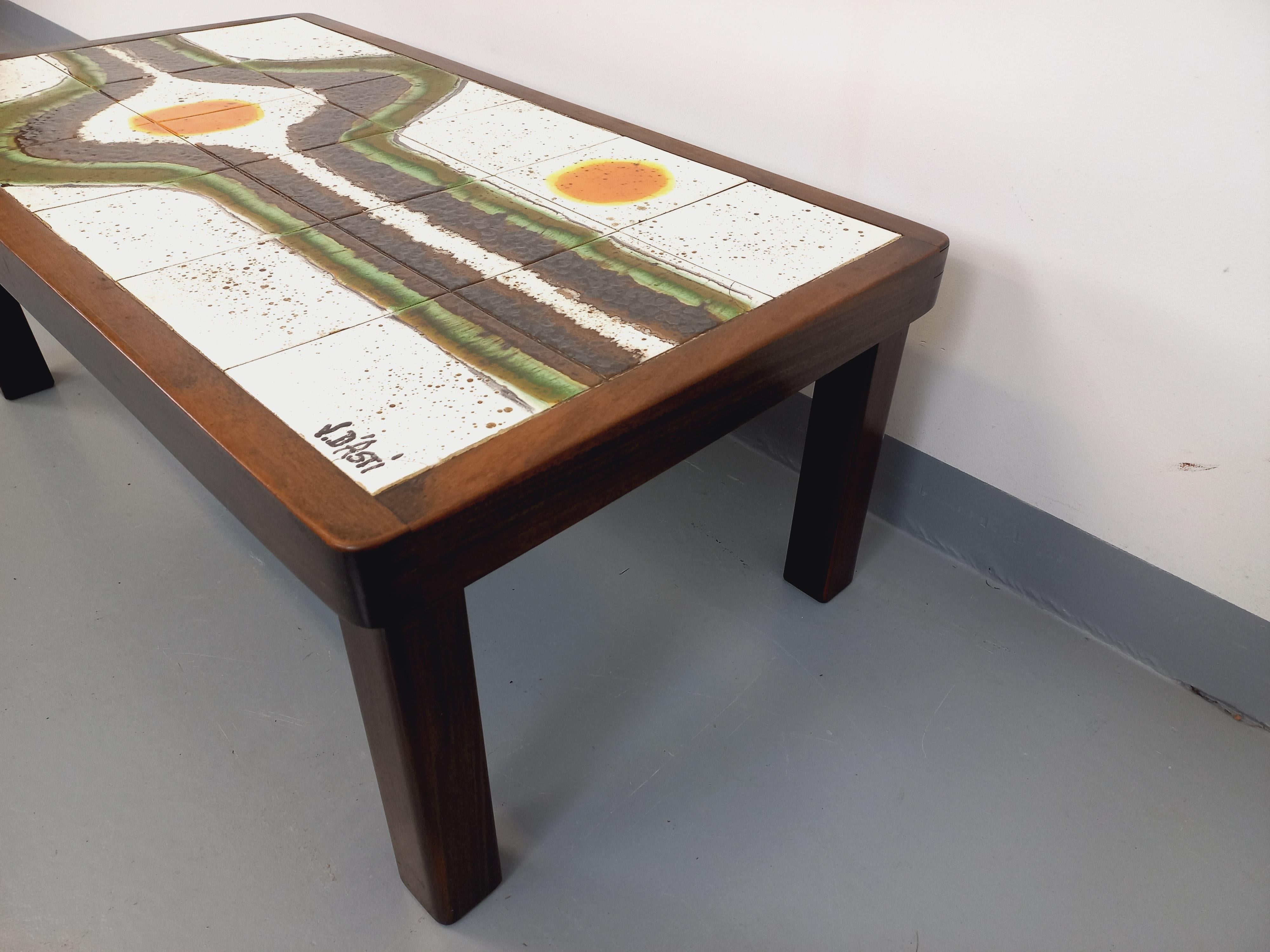 Table basse vintage rectangulaire signée Jean d’Asti des années 60 70, piétement et structure en bois foncé, plateau en superbe céramique de Vallauris au décor abstrait dans les tons blanc crème, brun, vert amande, orange et jaune. Superbe design