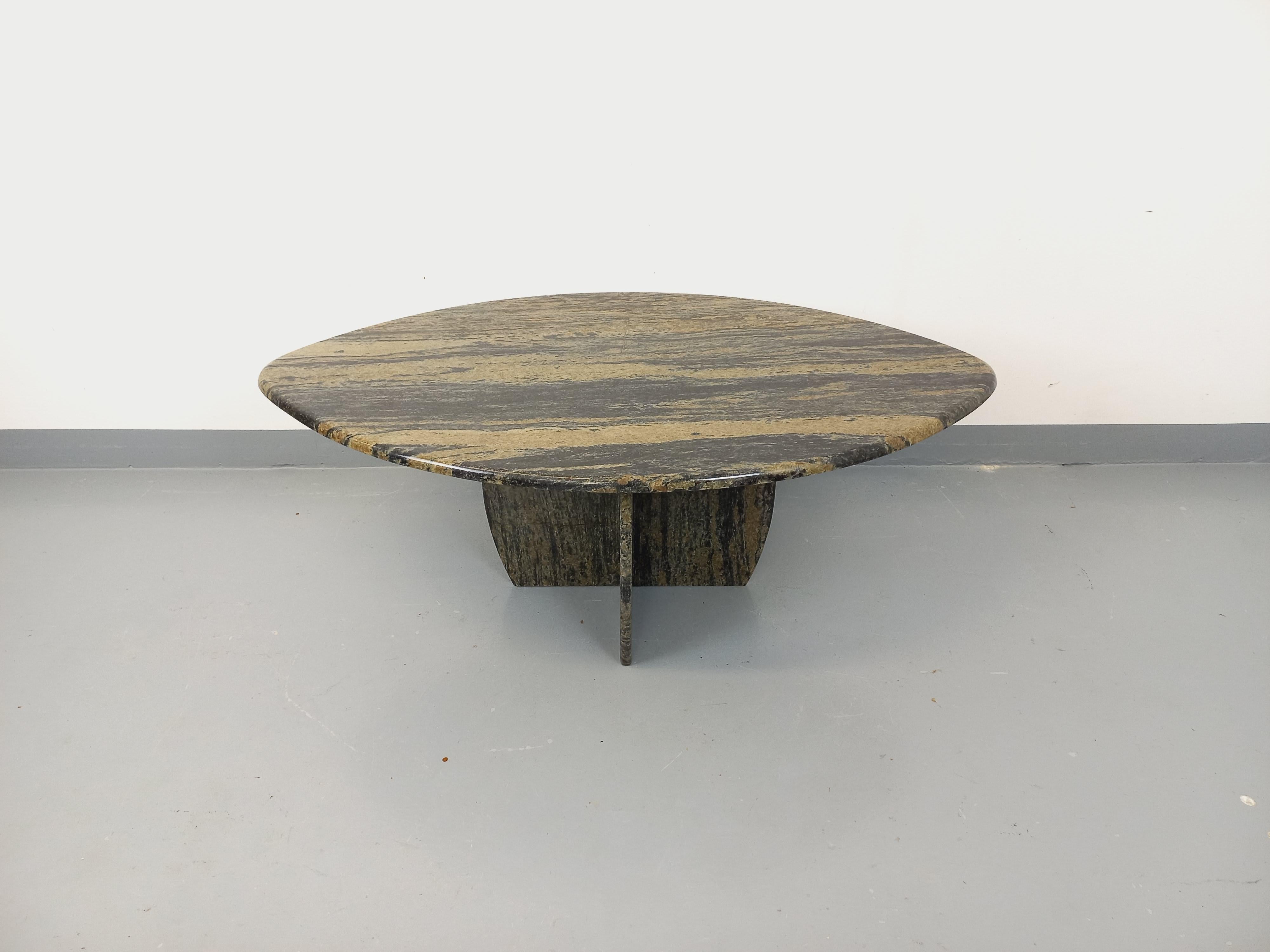 Table basse vintage des années 70, plateau en forme de double ogive ou ovale à deux pointes, pied central à quatre pans, en granit type marbre aux belles nuances de gris foncé et de greige, très bon état général avec micro-rayures d'usage et de