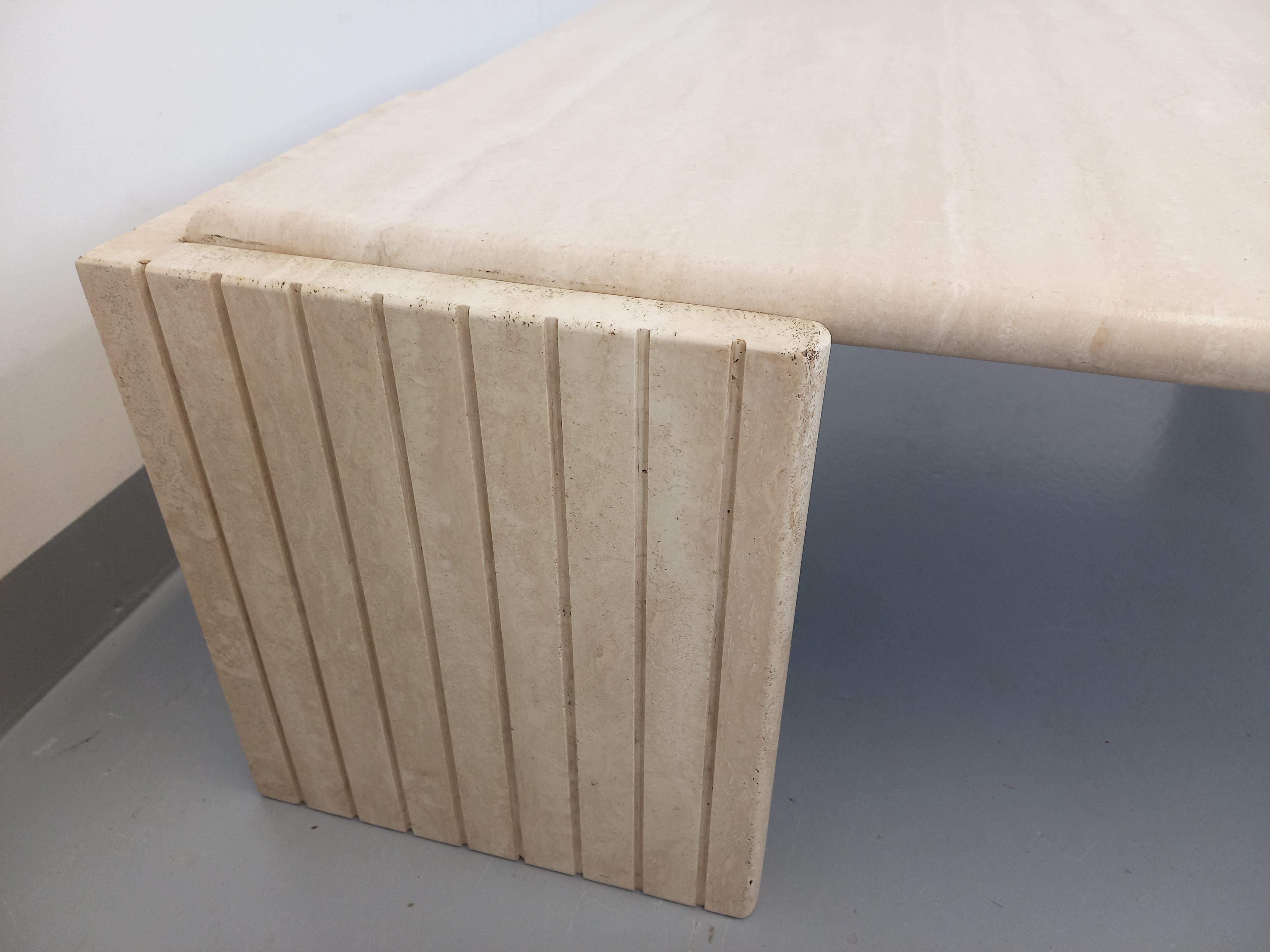Table basse vintage des années 70, en travertin, forme carrée arrondie sur deux angles (ou forme d'œil) et deux pieds d'angles rainurés. Superbe design, probablement de chez Roche-Bobois. Très bon état général avec quelques micro-rayures d'usage de