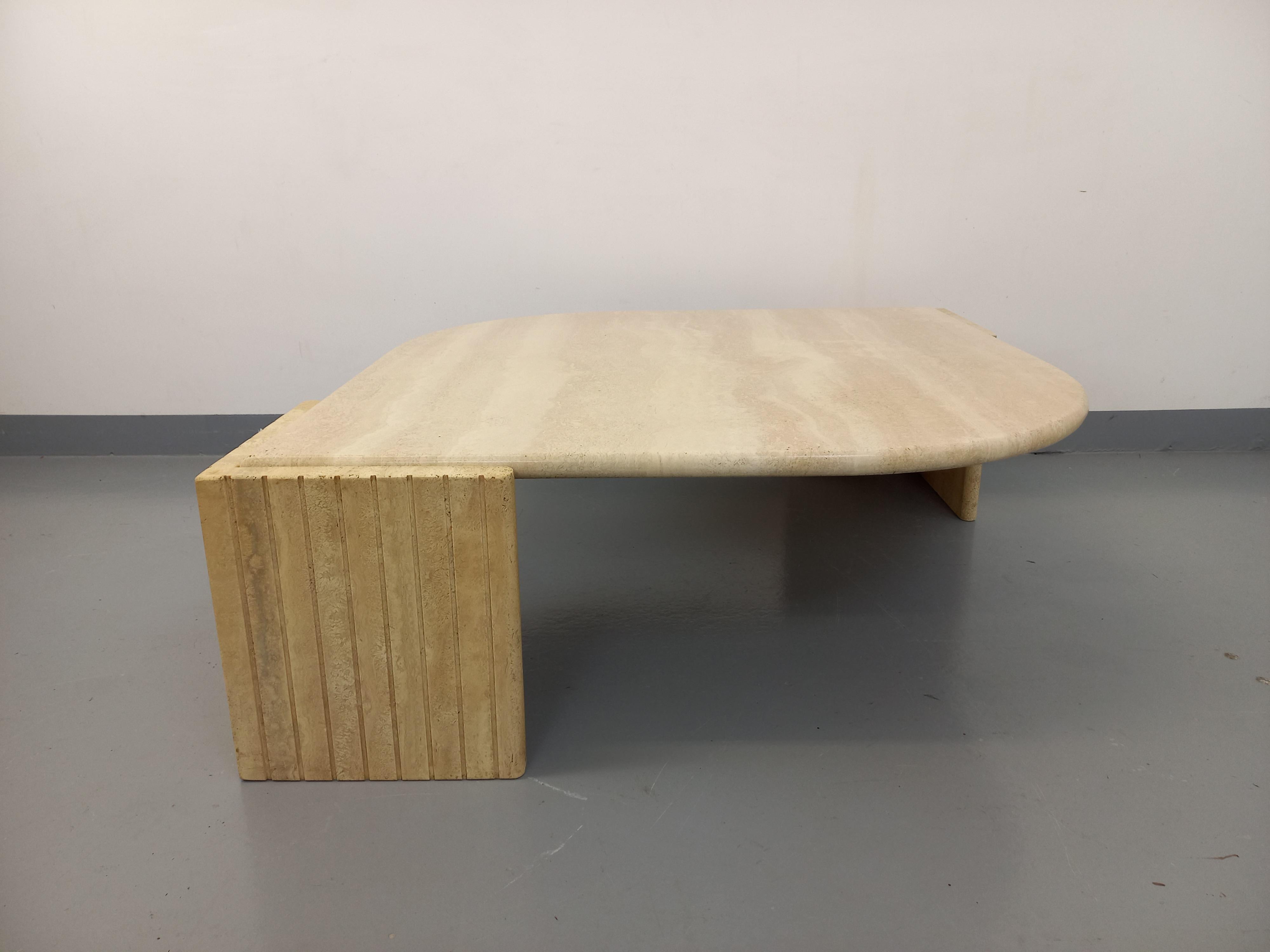 Table basse vintage des années 70, en travertin, forme carrée arrondie sur deux angles (ou forme d'œil) et deux pieds d'angles rainurés. Superbe design, probablement de chez Roche-Bobois. Très bon état général avec quelques signes du temps qui passe