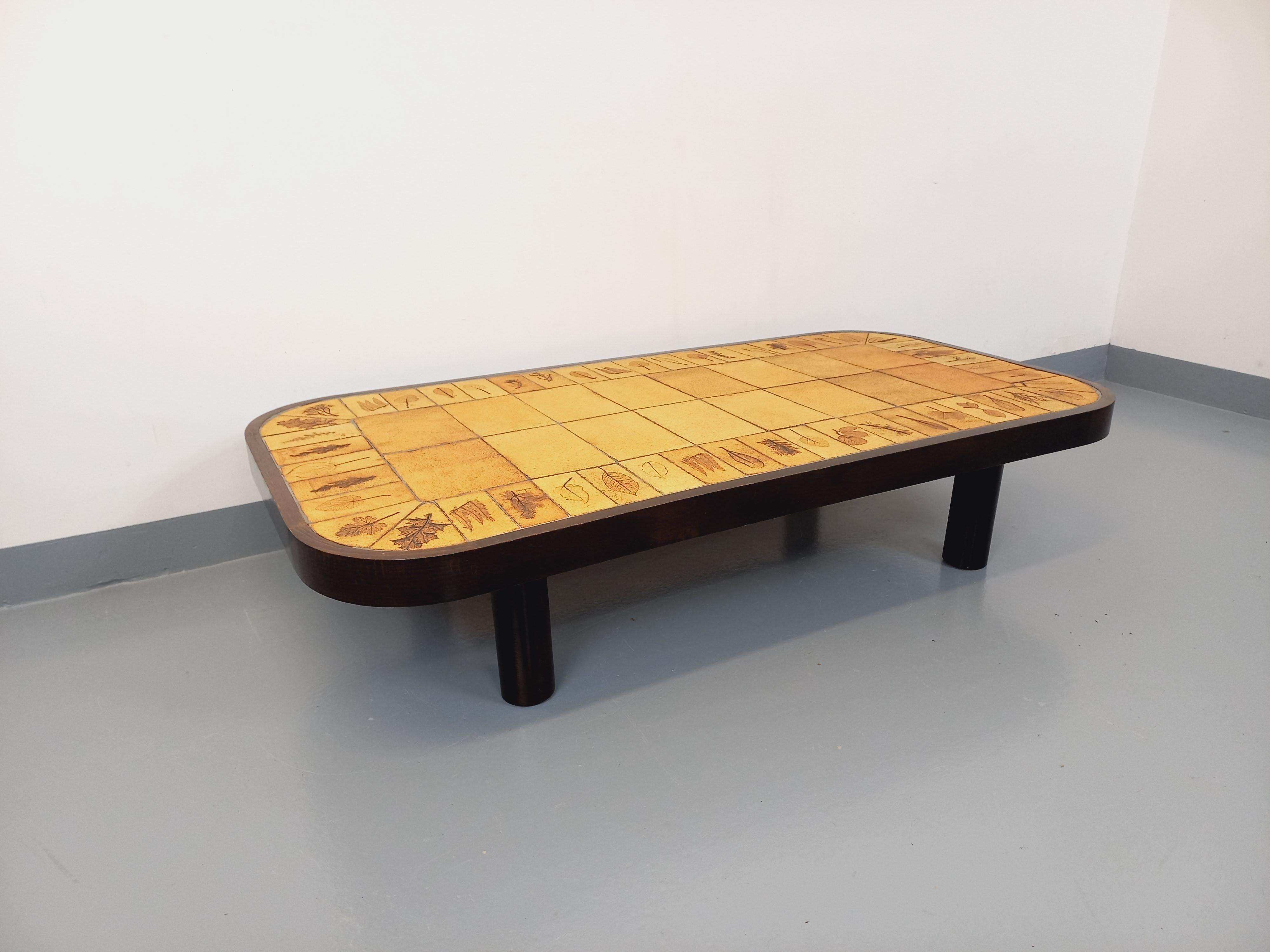 Grande table basse rectangulaire vintage Roger Capron des années 60 70, pieds ronds cylindriques et structure en bois foncé, plateau rectangulaire arrondi en céramique ocre de Vallauris motifs herbier, bon état général avec quelques signes du temps