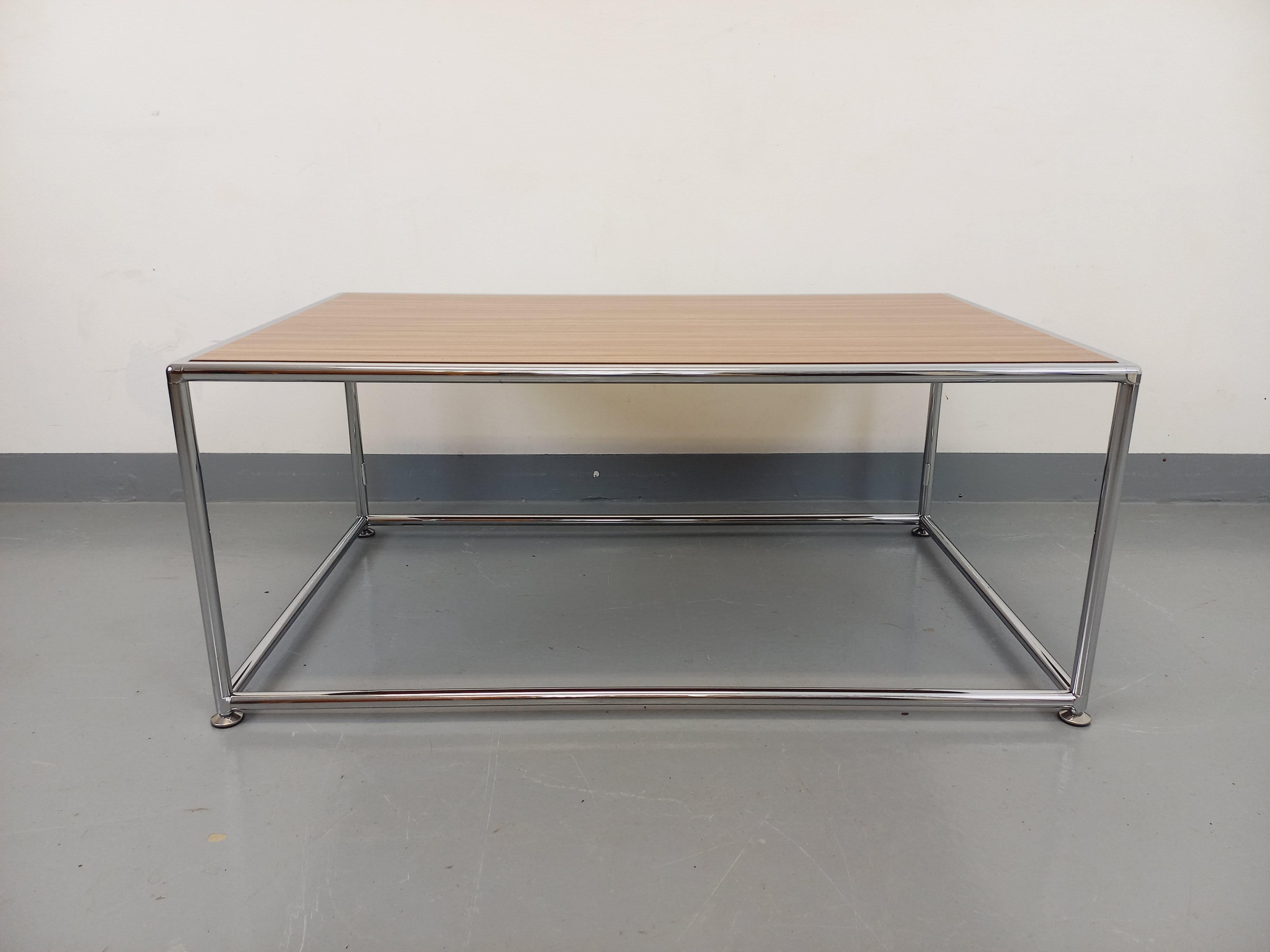 Table basse vintage dans le goût des meubles USM, plateau rectangulaire en mélaminé imitation bois, piétement en métal chromé au design tubulaire, très bon état général, chrome en très bon état, quelques rares micro-rayures d'usage sur le