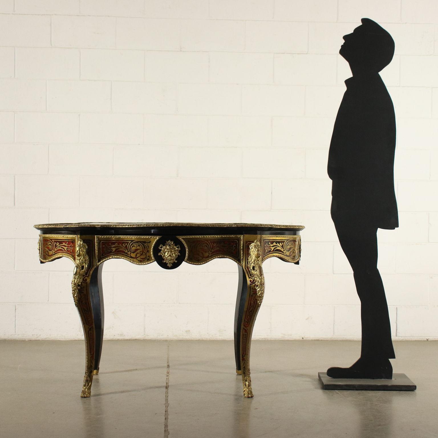 Boulle style table supported by curved legs, the under the top band is shaped. The piece of furniture is entirely inlaid in the Boulle style, with golden phytomorphic volutes on a fake tortoiseshell background; enriched with bronze shoes and