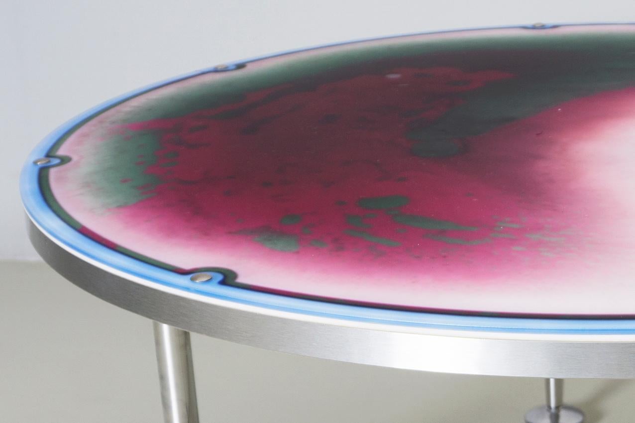 Table unique et ludique de l'artiste Bruno Contenotte. Plateau de table en plastique mat et transparent rempli de liquide coloré en violet et vert, bord circulaire bleu et structure en aluminium, pieds chromés.

Bruno Contenotte, nom de scène de
