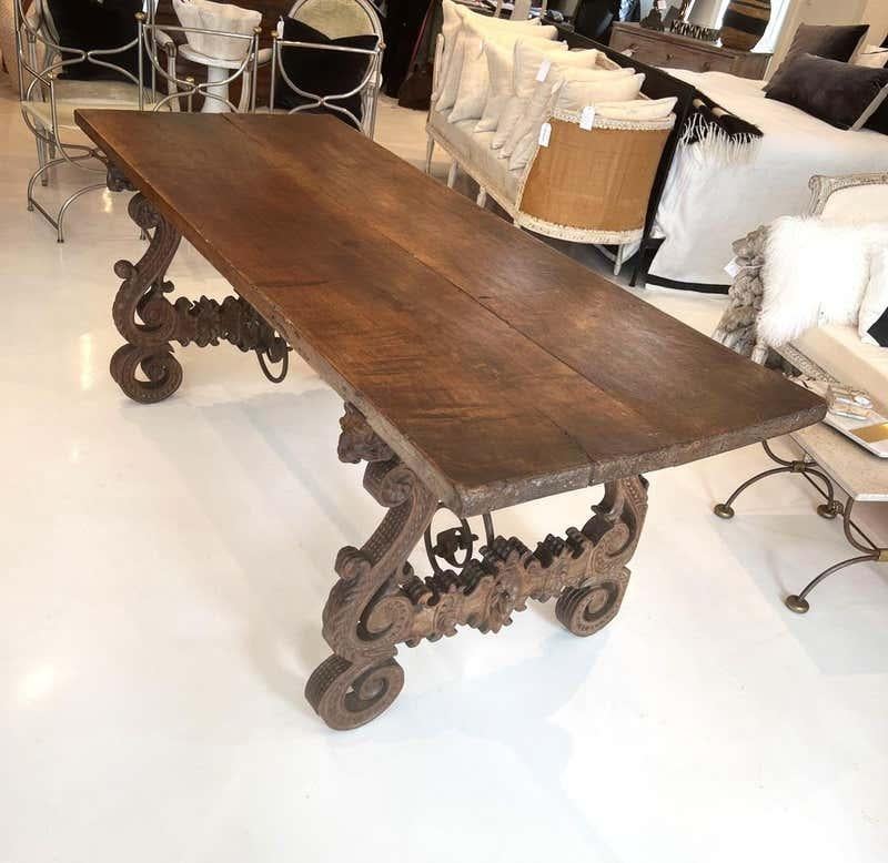 This is a very appealing trestle type table with a substantial top supported by remarkable legs. They are heavily carved, extremely ornate, and feature faces of a mustachioed (or frowning/grumpy) man's face at each corner. Curling and curved iron