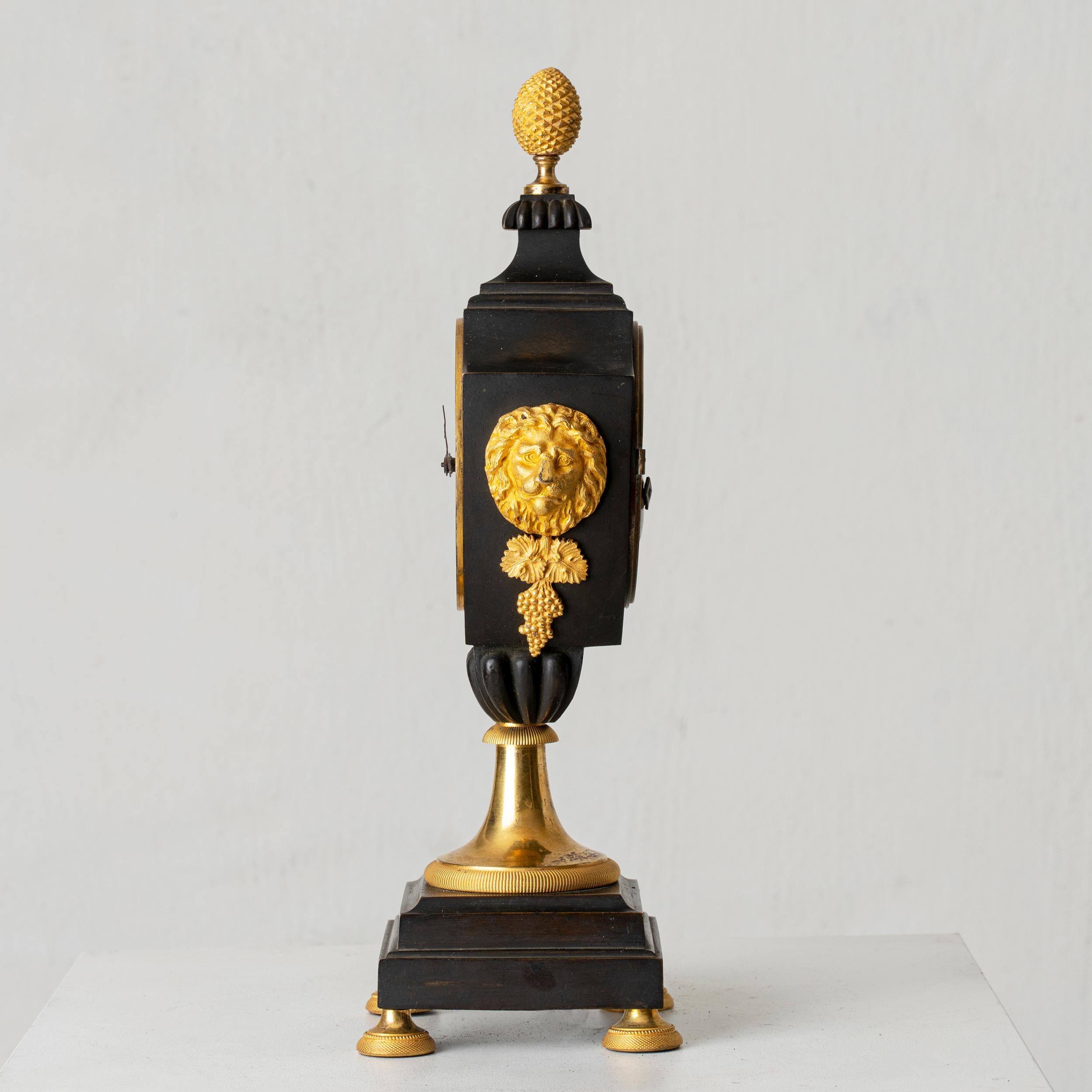 A table clock made in France during the Empire 1790-1820. Made from blackened wood and burnt-gilt bronze. Godronned urn-formation, lion mascarons, pine cone all Empire attributes