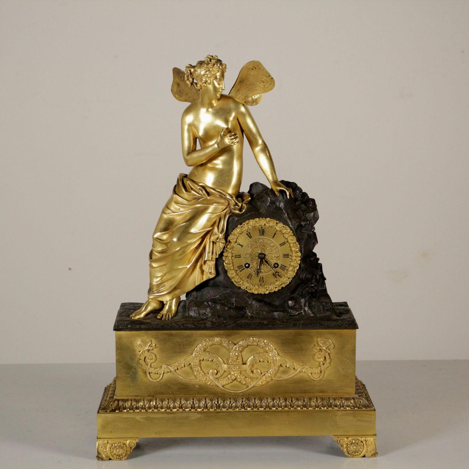 A table clock made of chiseled and gilt bronze with a rectangular basement supported by feet with studs enclosed in leaf volutes. Upper decoration with vegetable volutes, wreaths of flowers, rope and butterflies. The bronze second dial with Roman