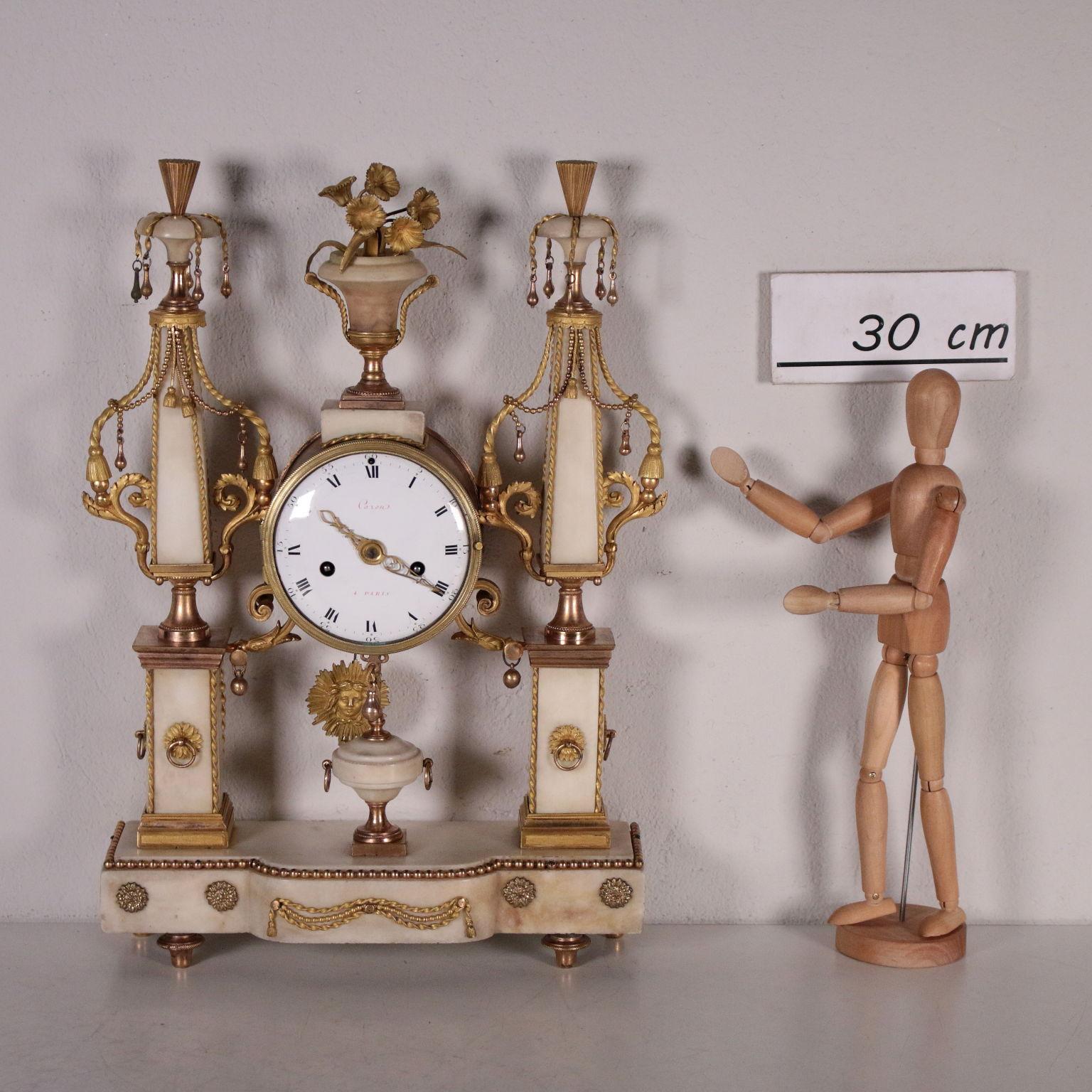 White marble clock with gilded bronze decorations. Two columns with square base stand on the rectangular basement, in the middle of the columns there is the cylindrical shaped clock. The white marble is enriched by decorations in gilded bronze,