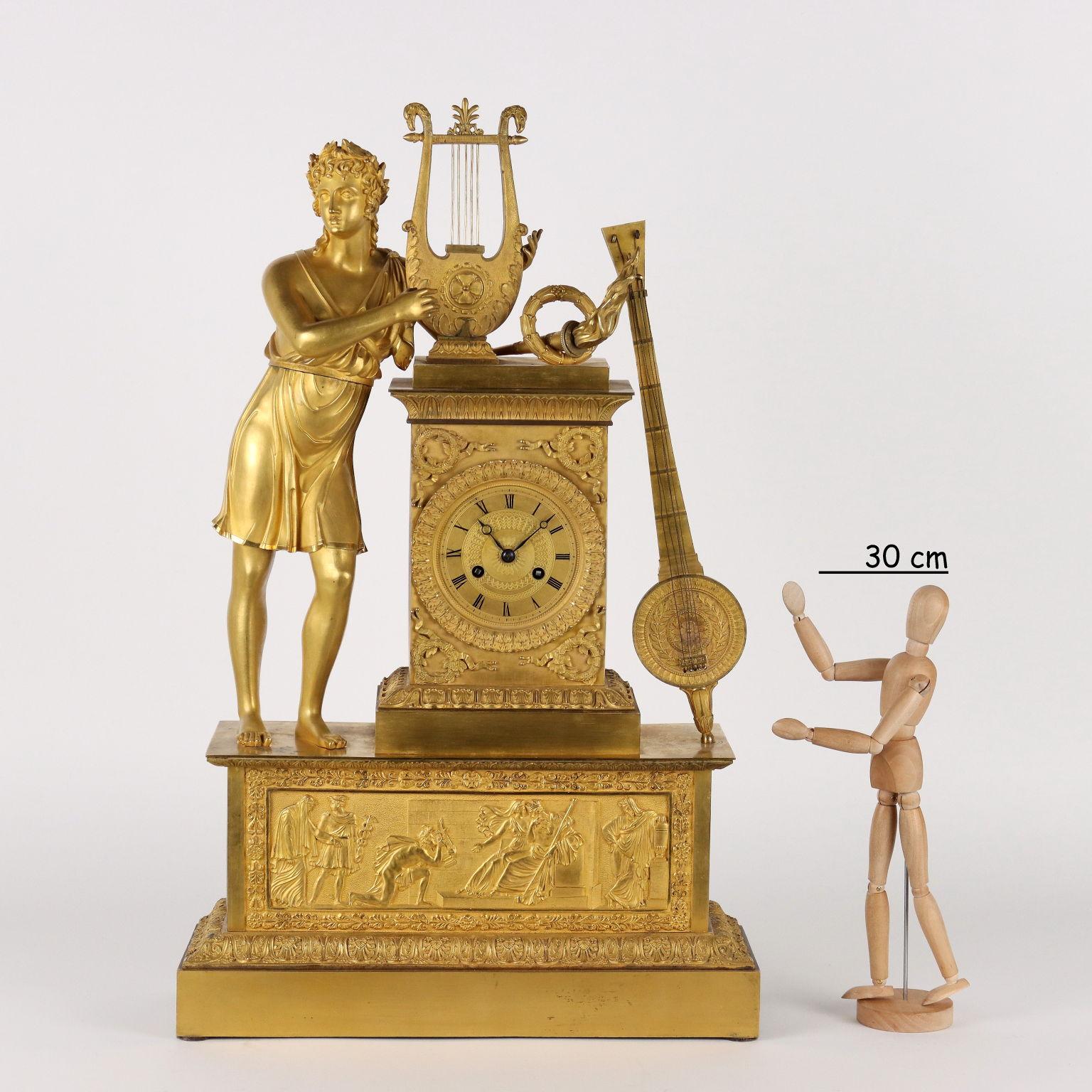 Gilded and chiseled bronze clock. On the large rectangular base there is a scene with mythological divinities in relief on a finely chiseled background. Decorations with plant motifs and repeated motifs. The clock is surmounted by a large statue