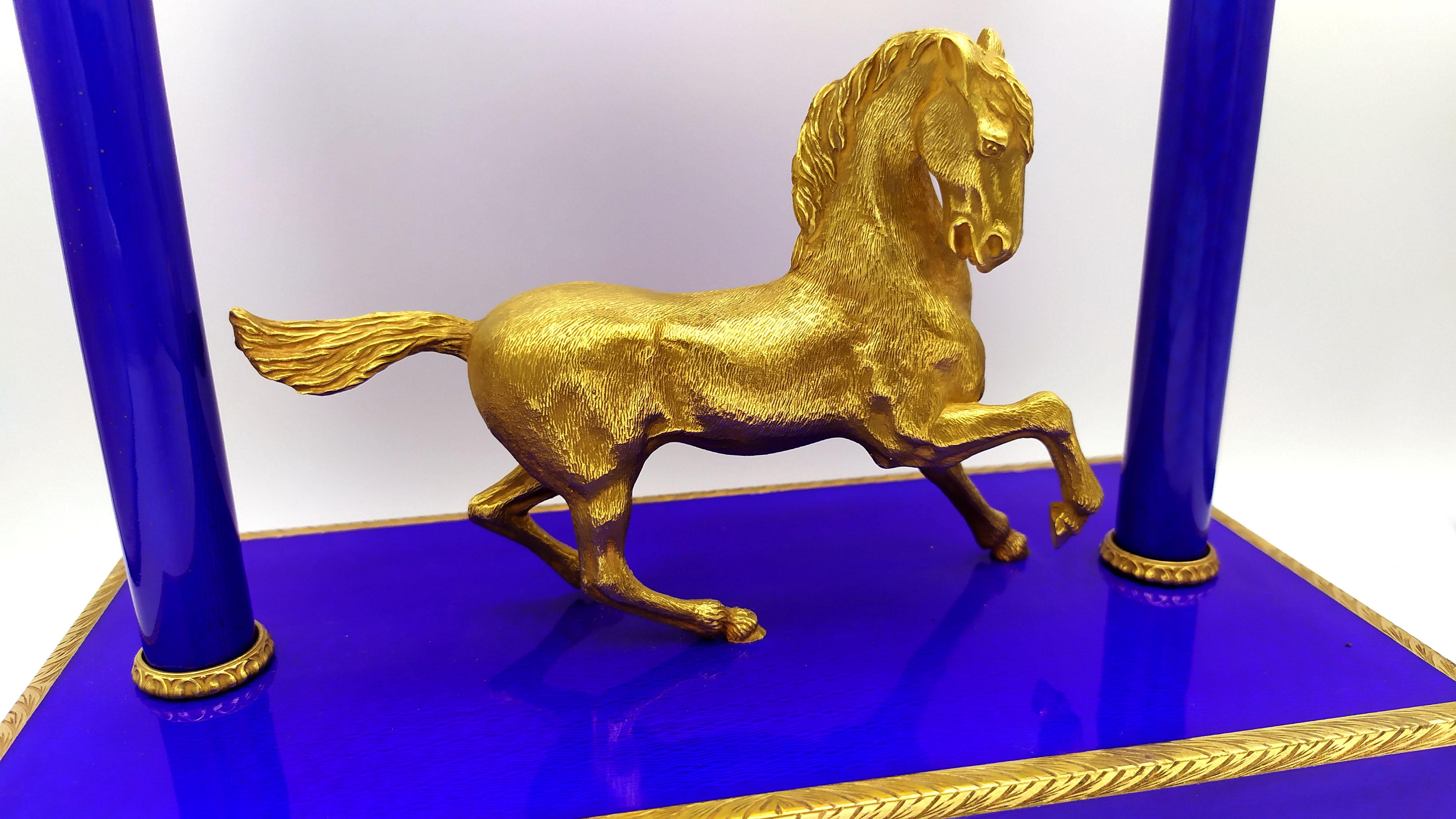 Large table clock in 925/1000 sterling silver gold plated with translucent fired enamels on guillochè, formed by a rectangular base of cm. 12 x 24 x 4 mounted on lion's paw feet on which rests a lively horse sculpture of cm. 11 x 15 and two columns