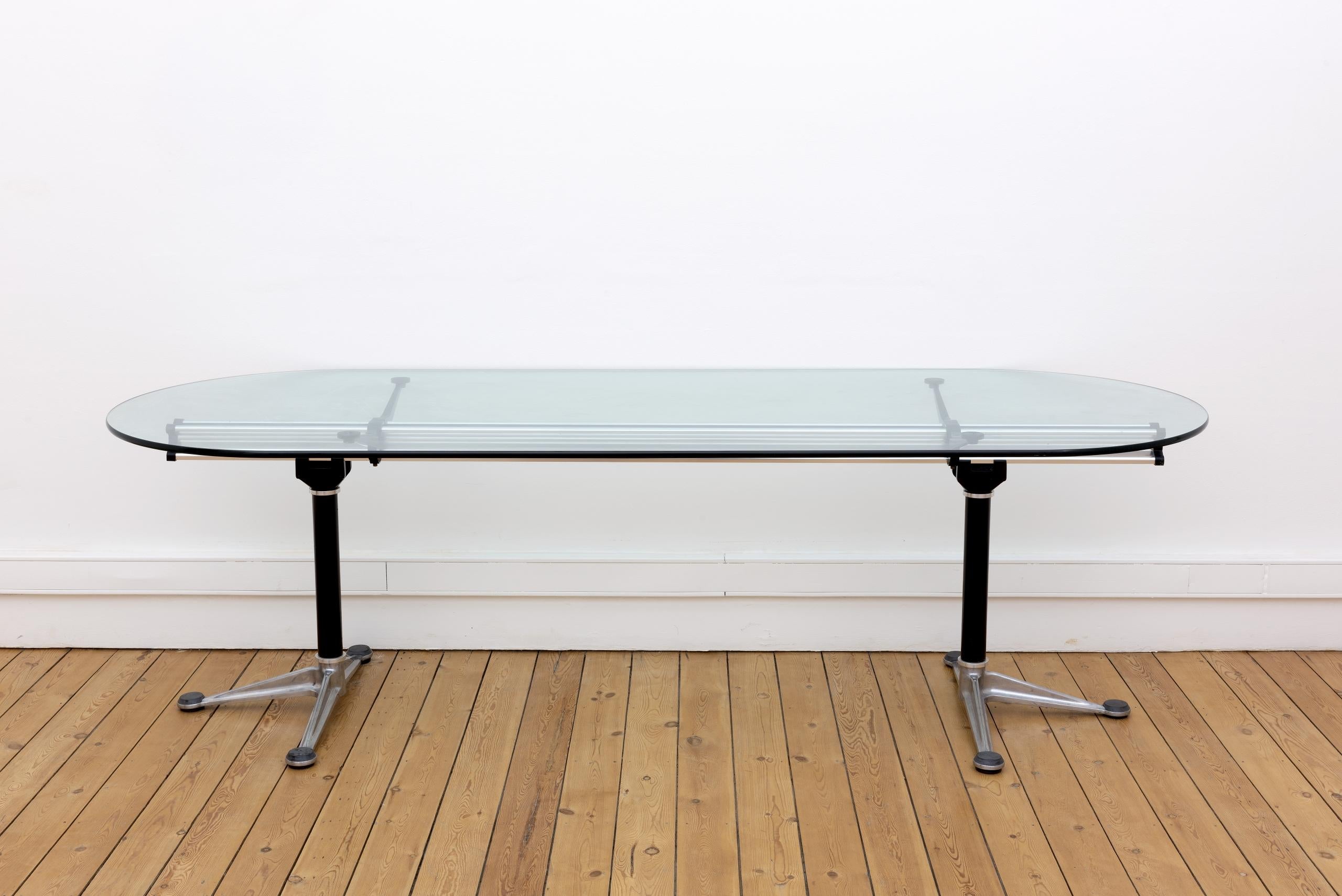 Une poutre centrale unique en aluminium confère à cette table conçue par Bruce Burdick un profil saisissant.

Les “tables Burdick” sont considérées comme des “classiques contemporains”.

L’épaisseur des plateaux en verre à bord arrondi est de