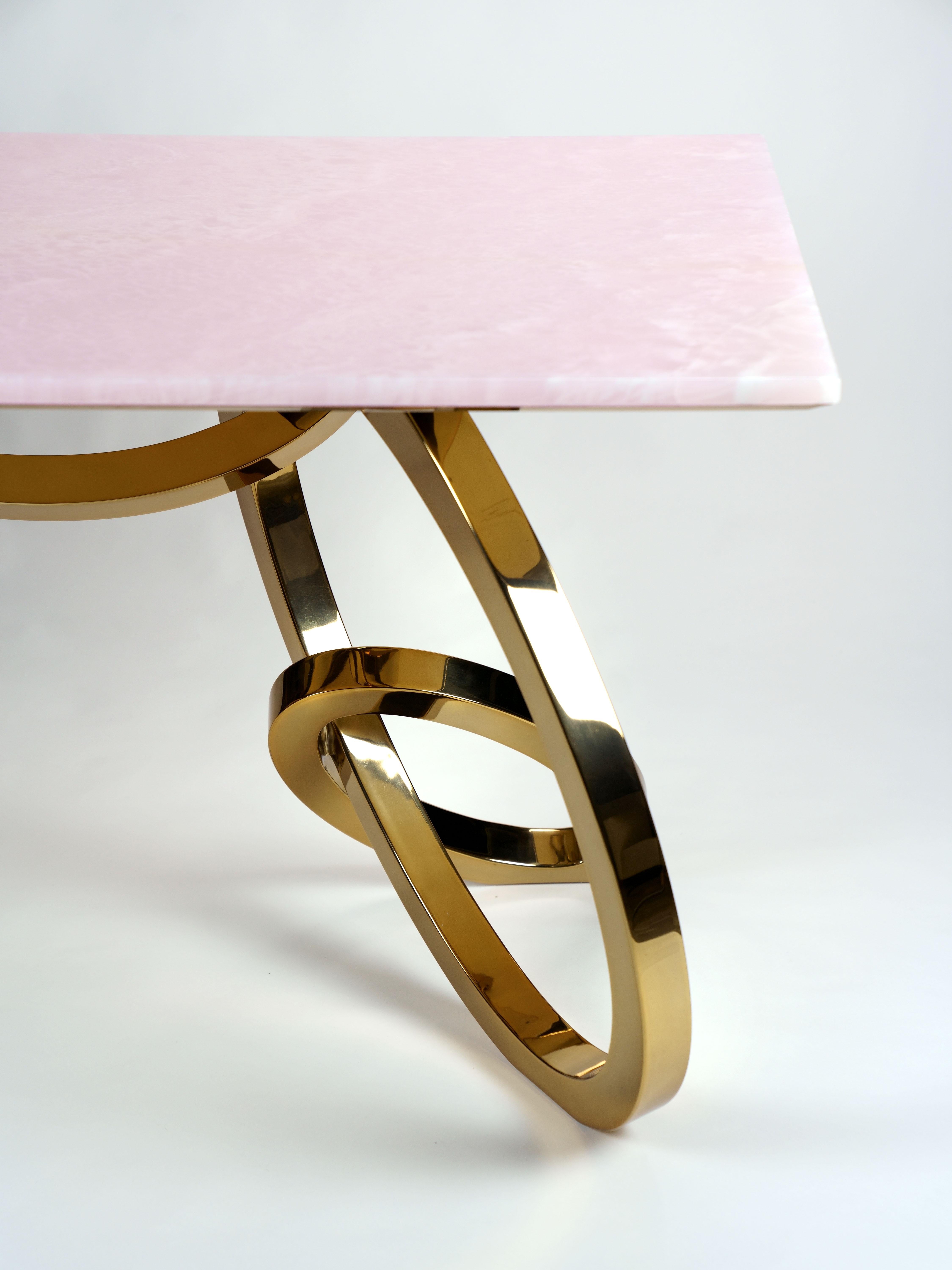 La table 'Bangles Desk Gold' est un bureau important avec une structure en acier inoxydable poli miroir avec une finition spéciale galvanique en or 24 Kt et un plateau en onyx rose rare. La finition galvanique de l'or 24 Kt peut être plus ou moins