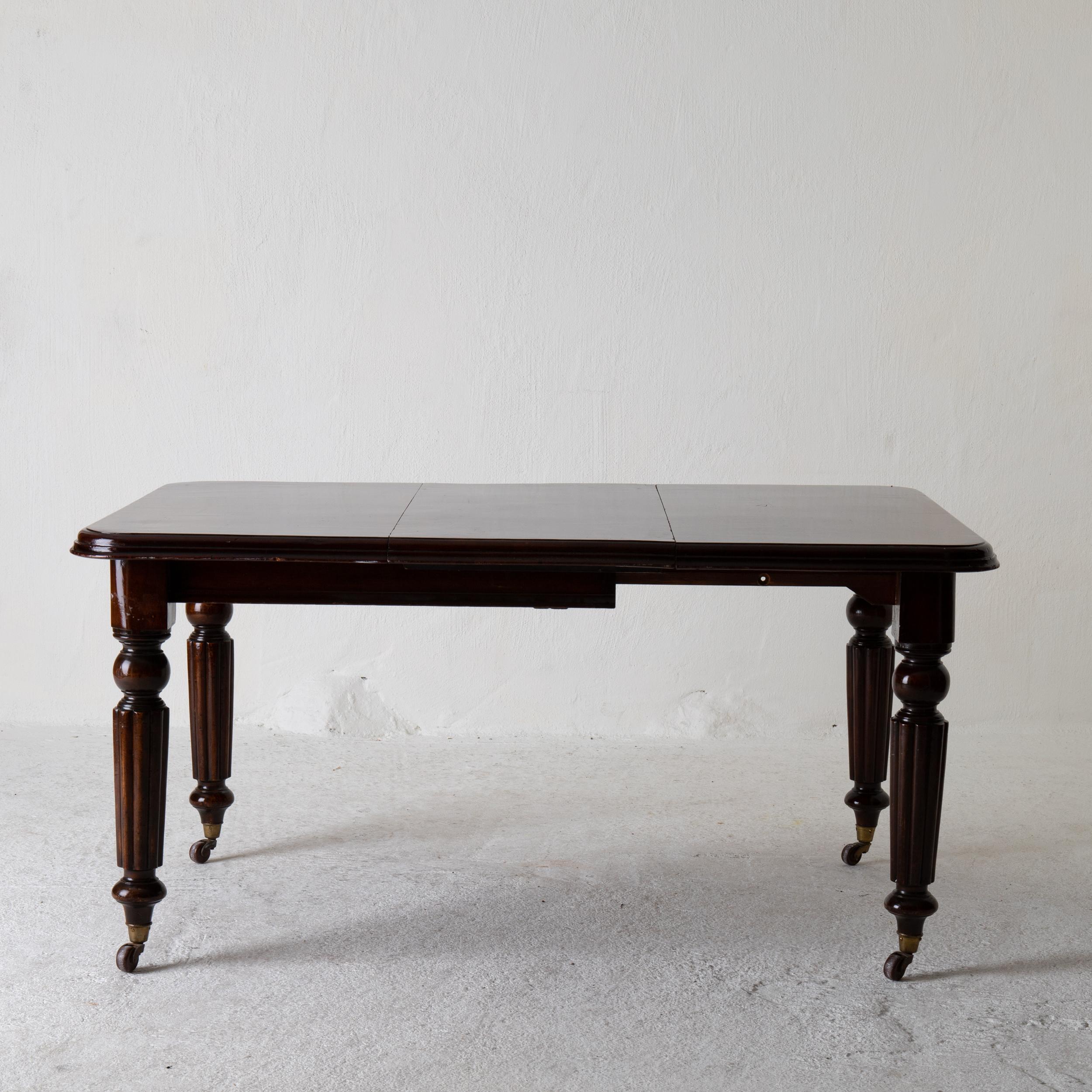 Table dining table English dark brown mahogany 19th century England. A table made during the 19th century in England. Made in dark mahogany. Extendable top with one leaf and rounded corners. Round and channeled legs standing on brass casters. Leaf: