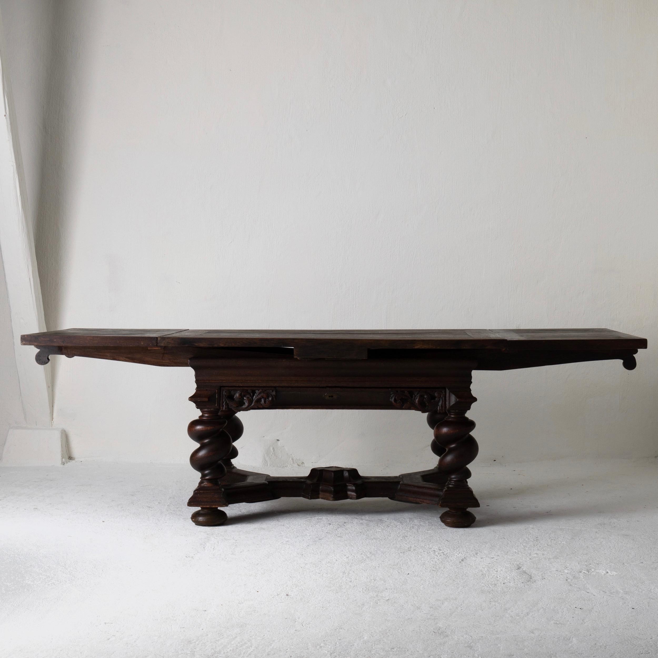 Table made in Sweden during the Baroque period 1650-1750. Made in dark stained oak. Two extendable leaves a 21.5” each. Base with a wide drawer and foot cross. Beautiful carvings and original locks. Each leaf is 21.5