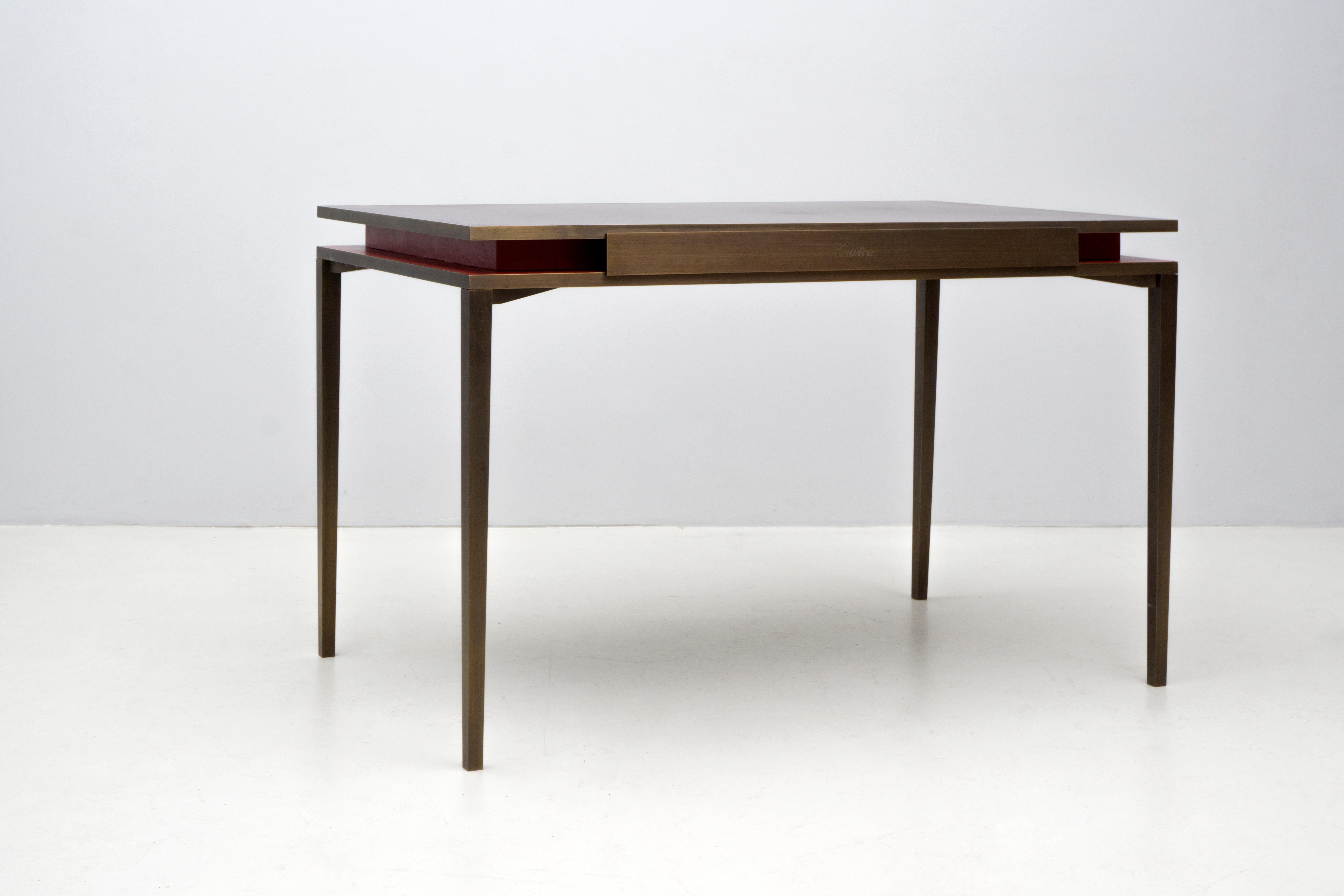 The table was manufactured by John Desmond LTD UK for the french luxury company Cartier Paris. It consists of two levels, the bottom one being covered in red leather and the top one in aubergine-colored leather. The table itself is made of