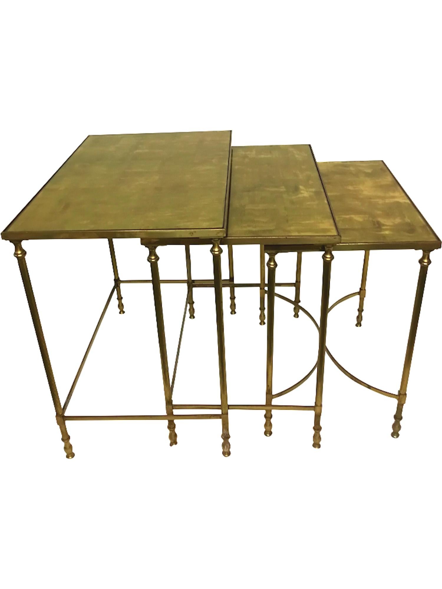 Vintage set of 3 neo classical style nested tables in gilt bronze with fluted legs and arched stretchers on the smallest table and removable glass tops with gold leaf fixed under glass, in the style of the French design houses like Maison Jansen and