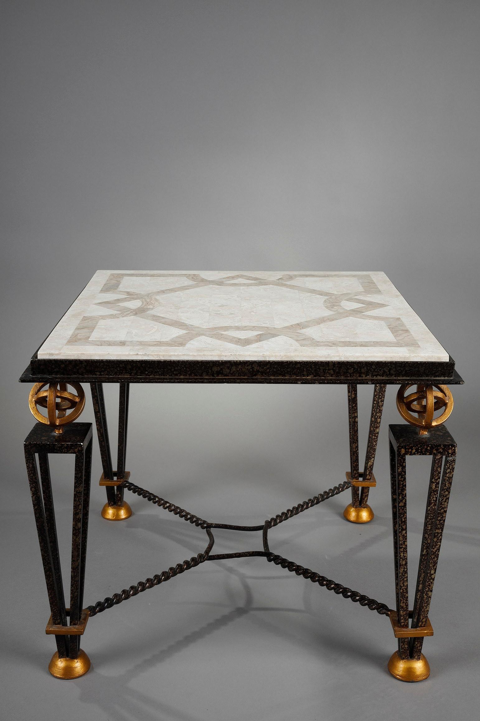 Small table in the taste of Gilbert Poillerat (1902-1988) in lacquered, gilded and oxidized metal. The tray is realized in marquetry of stone of different shades with geometrical patterns. The table rests on four feet in inverted openwork pyramids
