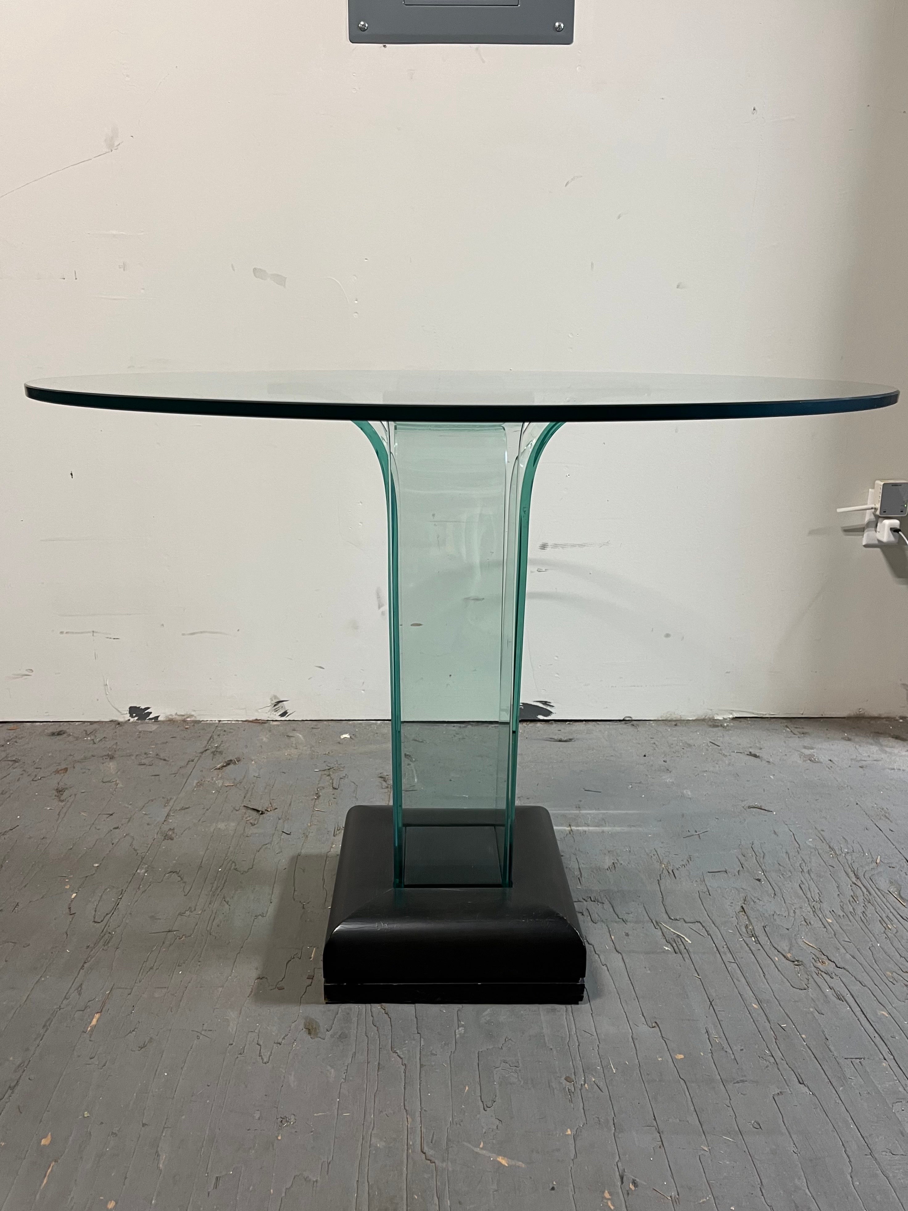 Ce superbe guéridon en verre, créé par le célèbre designer John L. Mathias, allie une élégance minimaliste à une forme sculpturale saisissante. Dotée d'un épais plateau rond en verre, la table est soutenue par un socle en verre incurvé unique qui