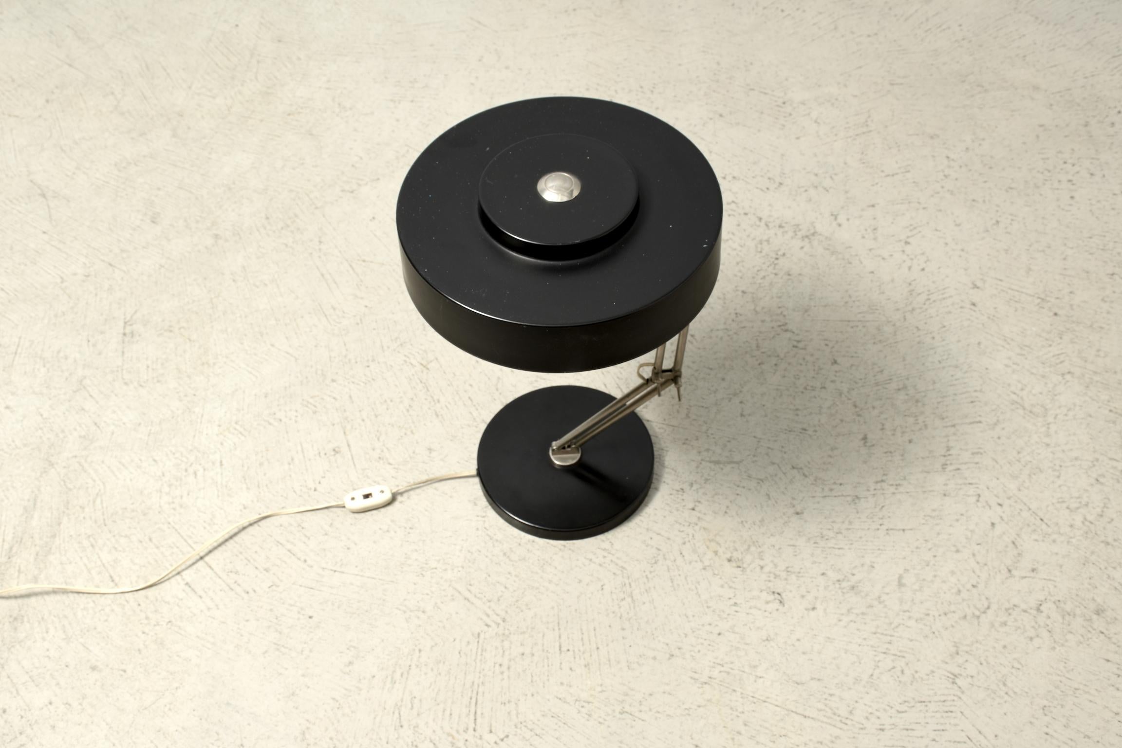 Table lamp, 1960s, with round shaped lamp shade in black painted sheet metal. Standing on a black sheet metal base. Two adjustable joint bars allow to move the lamp in different positions.