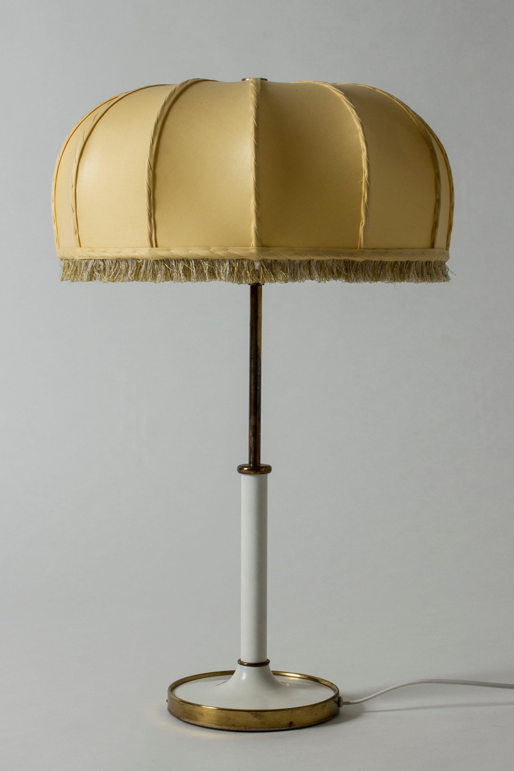 Beautiful table lamp by Josef Frank, model 2466. White lacquered metal base with a brass ring around the foot. Original billowy lamp shade with fringe around the edge.