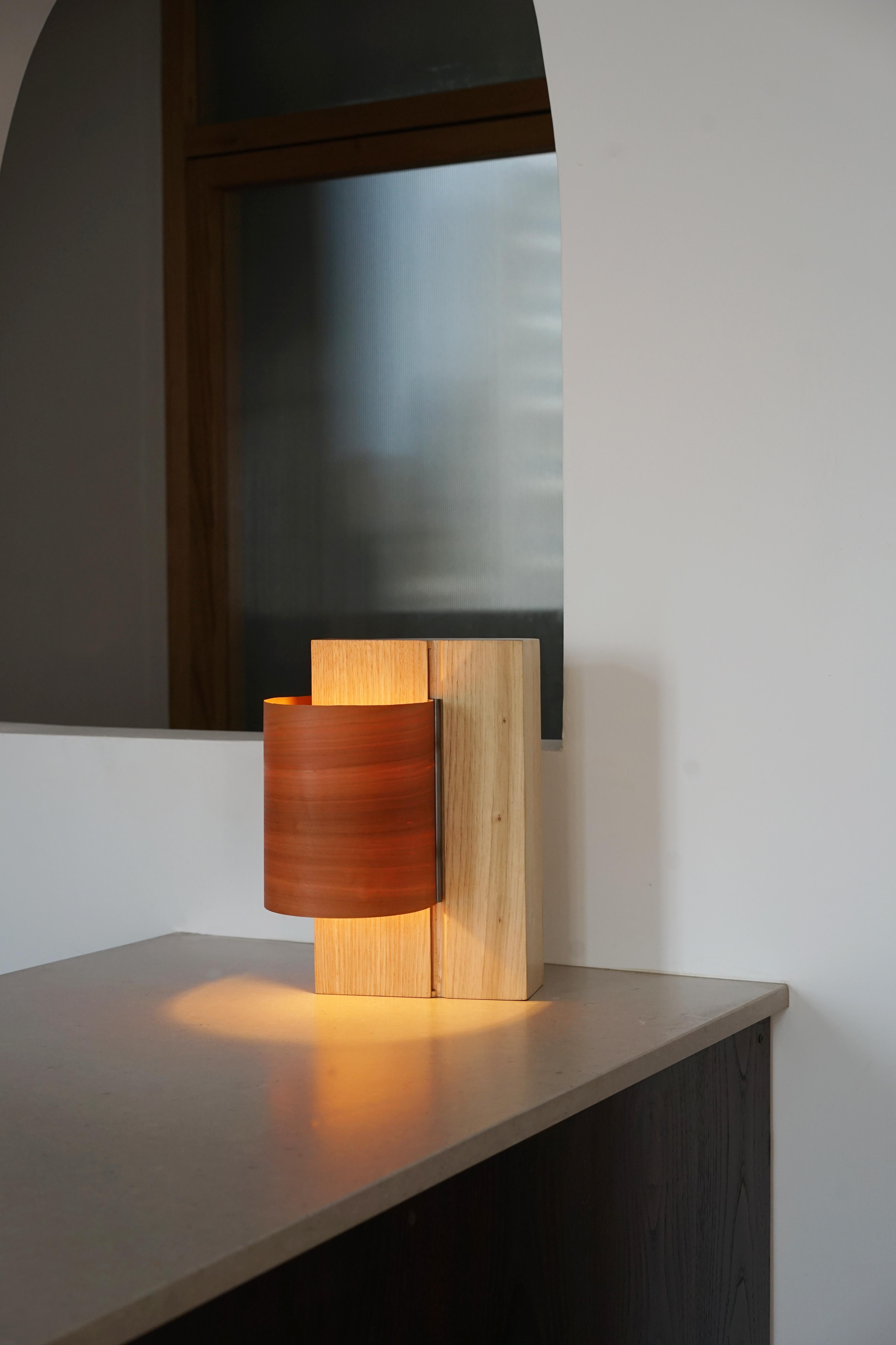 Cette lampe de table célèbre les qualités intrinsèques du placage de bois, en particulier sa finesse et son grain. Grâce à un système coulissant en acier inoxydable, la feuille de placage se déplace de haut en bas pour orienter la lumière selon vos
