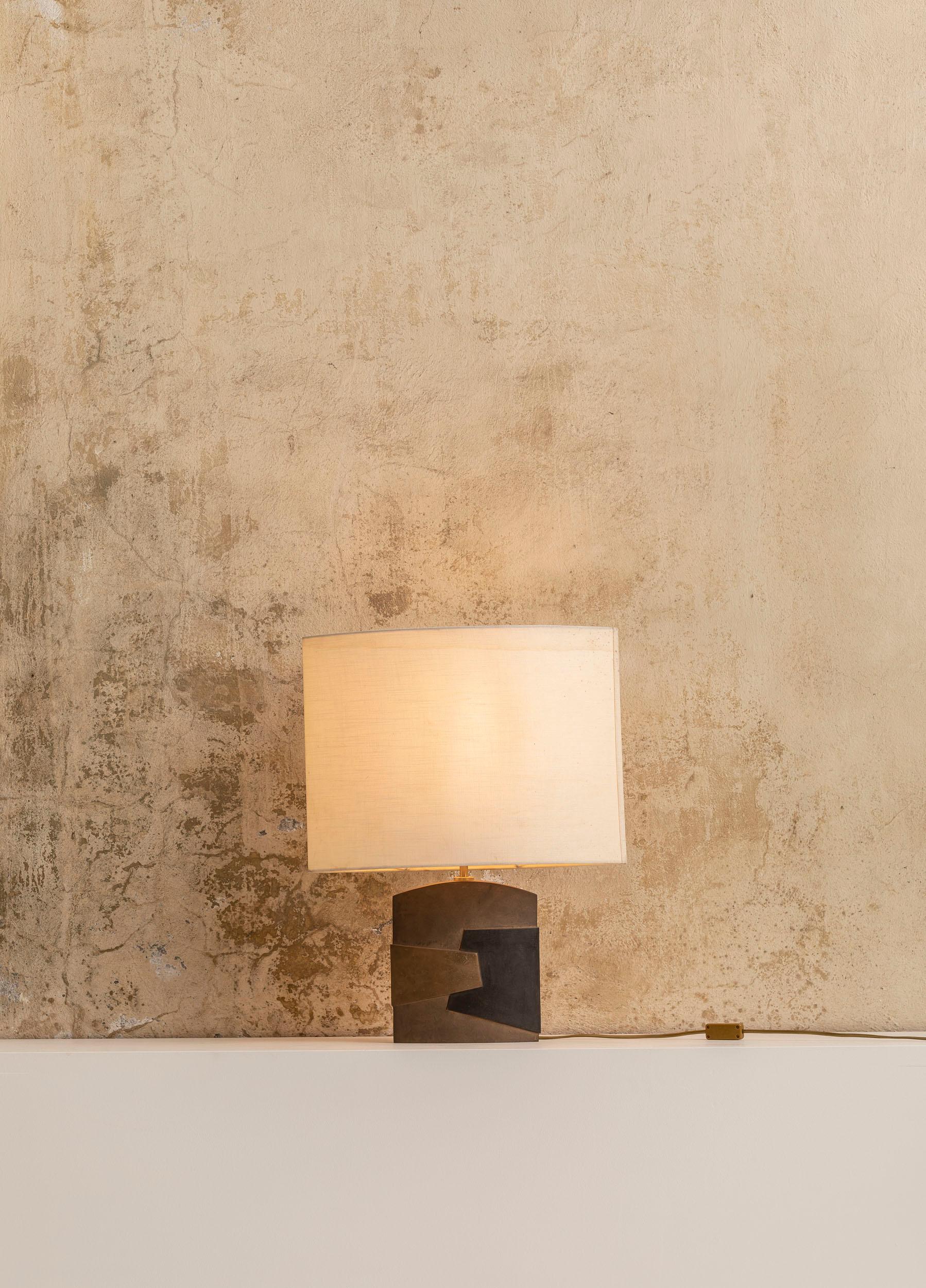 Table lamp by Esa Fedrigolli with a bronze base and an original shade.
The base presents a composition of geometrical elements in solid brass in three different colors. The original white shade has the same shape of the base, convex in the middle