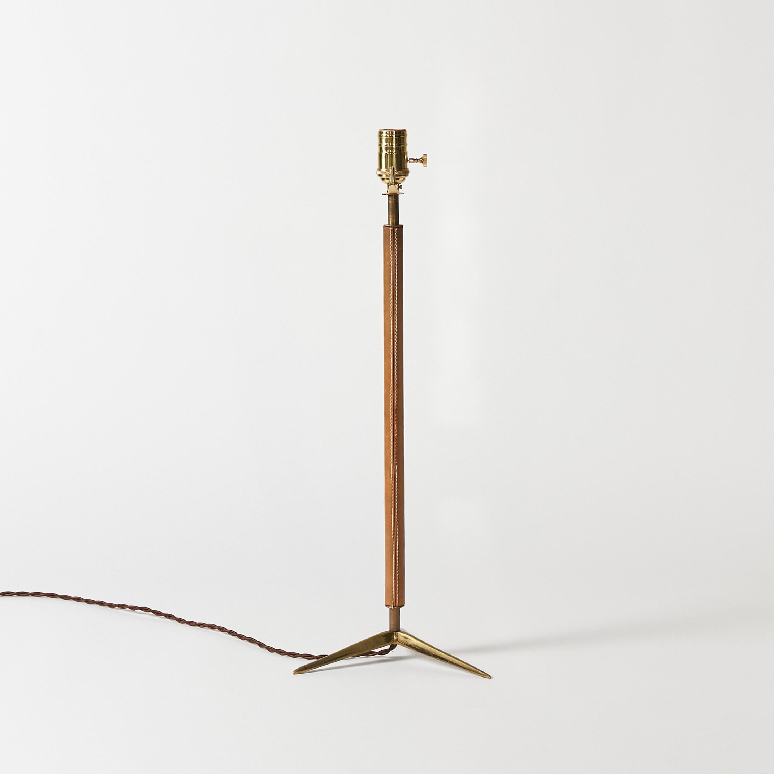 Table lamp base attributed to Jacques Adnet. Tripod style brass base and stem wrapped in saddle brown leather with contrasting stitching. Made in France.
This item has been rewired with new hardware and braided cloth cord. This lamp does not