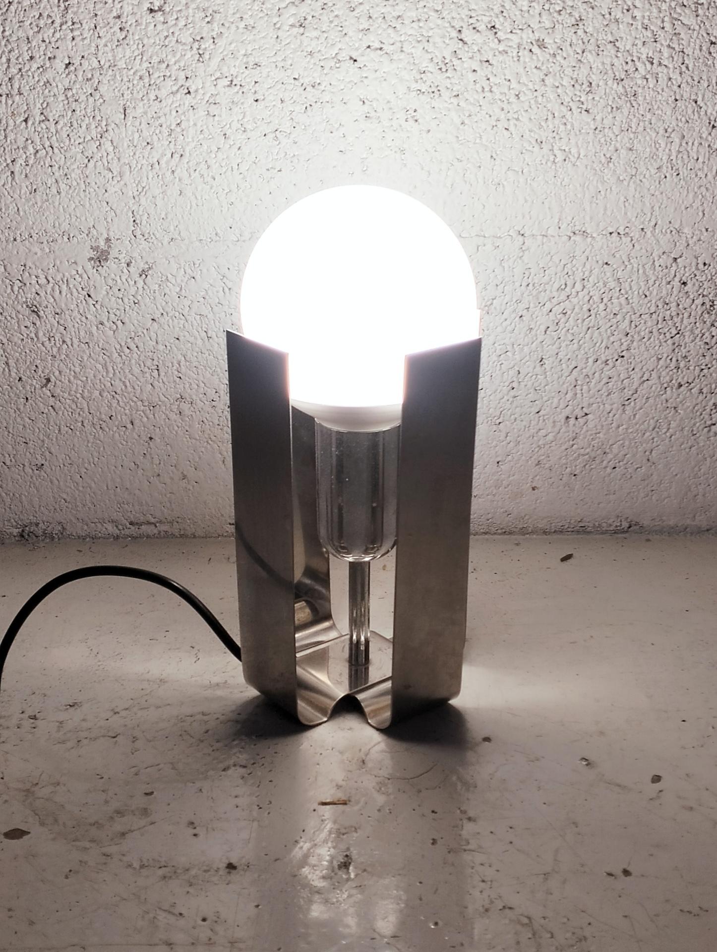 This table lamp was designed in 1971 by architect and designer Claudio Salocchi as part of his prolific collaboration with the company Lumenform. The minimalist but evocative design consists of two interconnected chrome-plated metal slats, onto