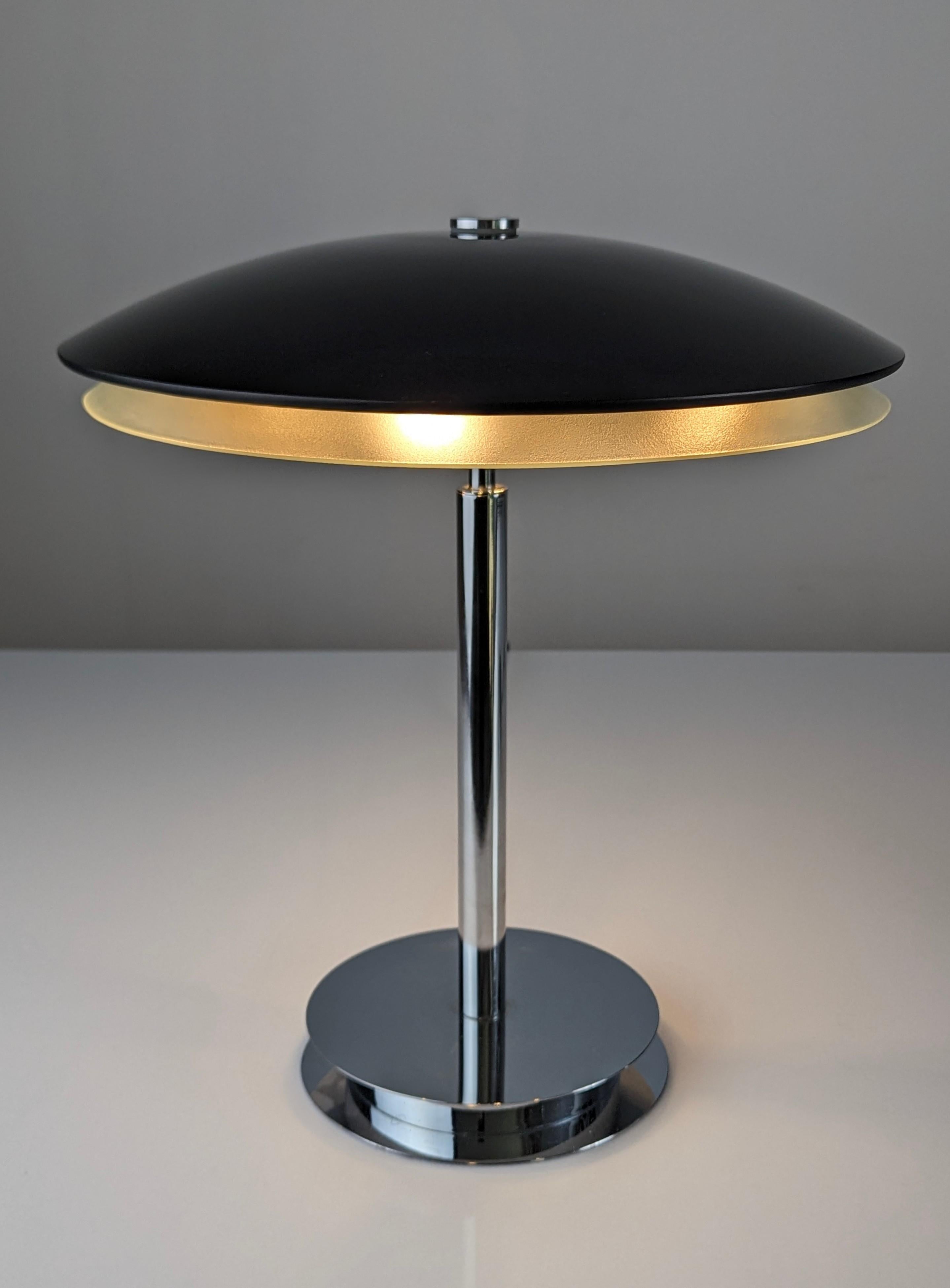 Elegante lámpara de sobremesa diseñada por Fontana Arte en 1954. Base bromada con parte superior de cristal doble curvado de color negro con reflejos rojo burdeos cuando está encendida, y parte inferior translúcida de color blanco que emite una