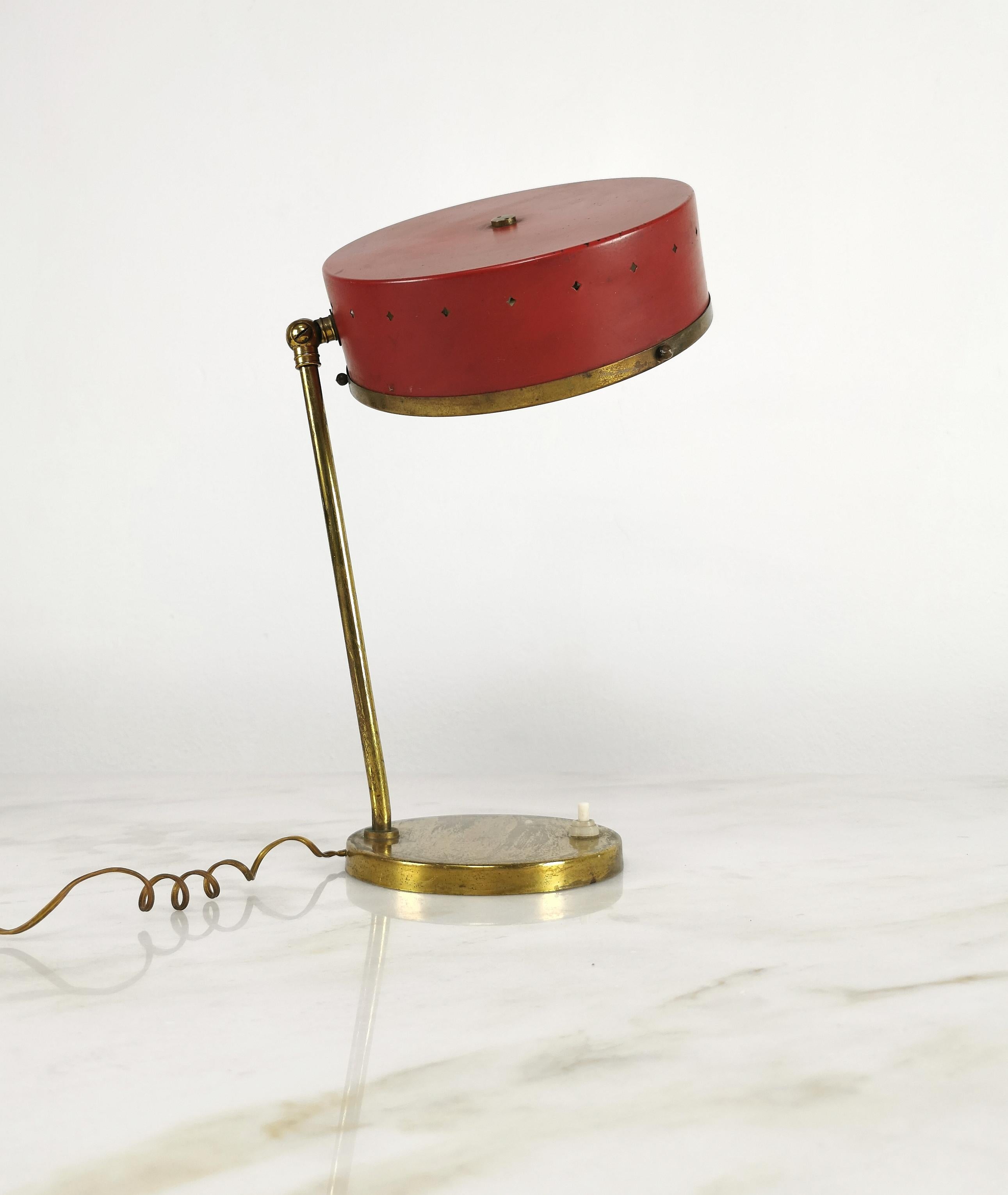 Lampe à poser  produite en Italie dans les années 1950, attribuée à Stilnovo. La lampe a été fabriquée avec une base circulaire en laiton où s'élèvent une tige et un joint en laiton, ce qui permet d'orienter le diffuseur en métal émaillé rouge avec