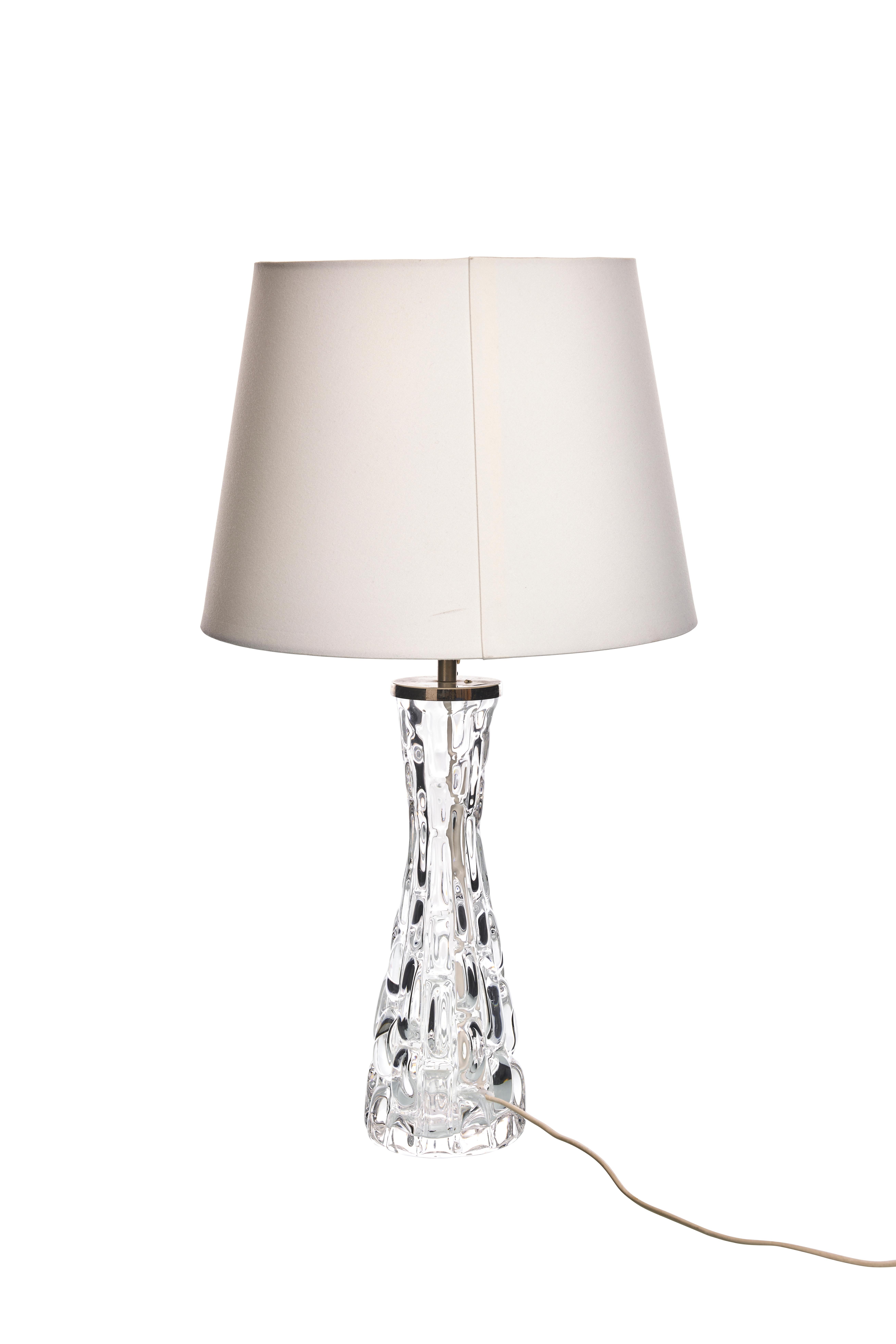 This table lamp, designed by Carl Fagerlund for Orrefors in the 1960s, features a clear, textured glass base with an intricate, droplet-like pattern. The exquisite craftsmanship of the glass base showcases Fagerlund's signature style, making it a