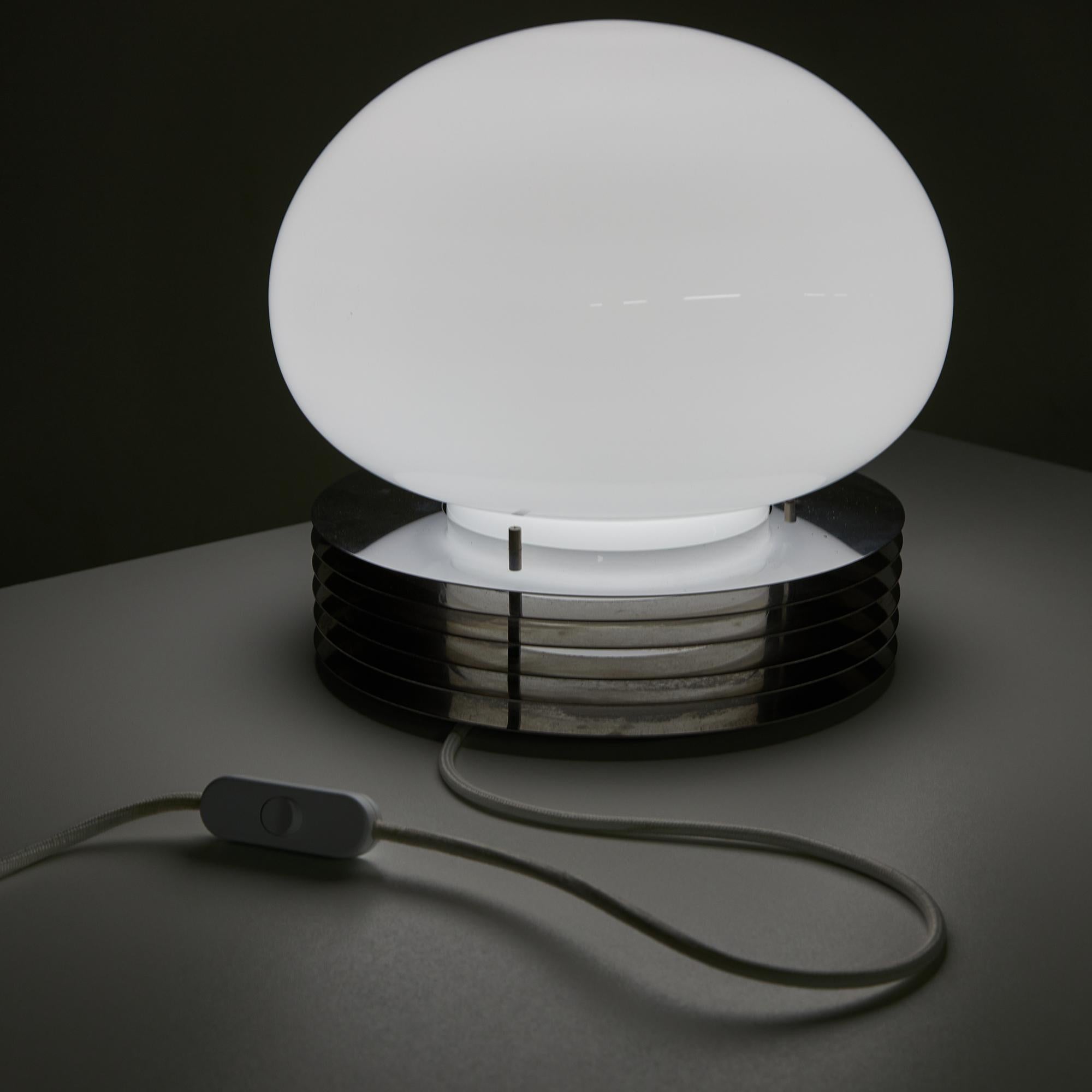 This stunning table lamp showcases a bold chromed steel base elegantly complemented by a beautifully crafted white flattened sphere made from genuine Murano glass. Designed by Enrico Tronconi for Tronconi in the 1970s, this piece embodies the spirit